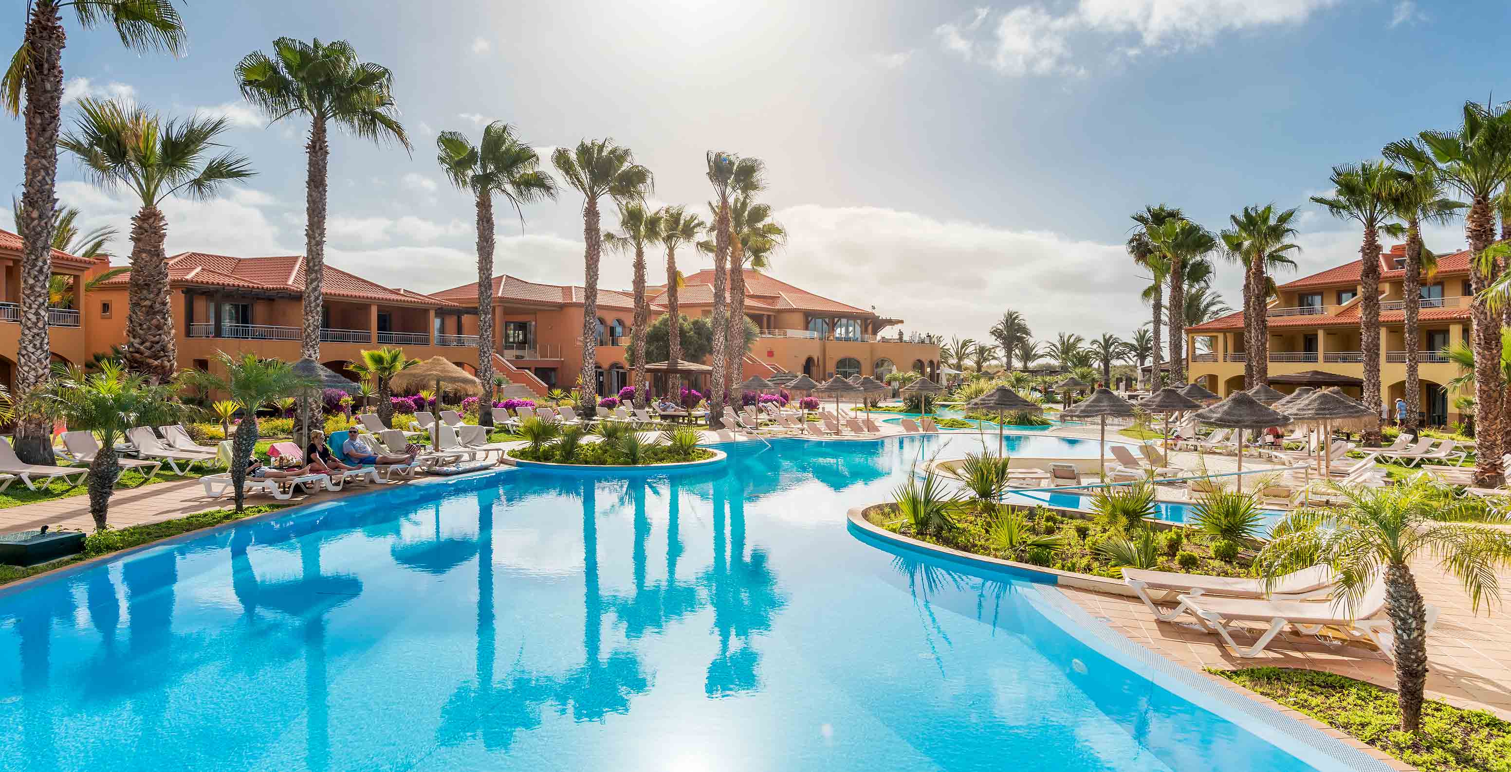 Large blue Pestana Porto Santo pool, loungers, palms, buildings under sunny sky