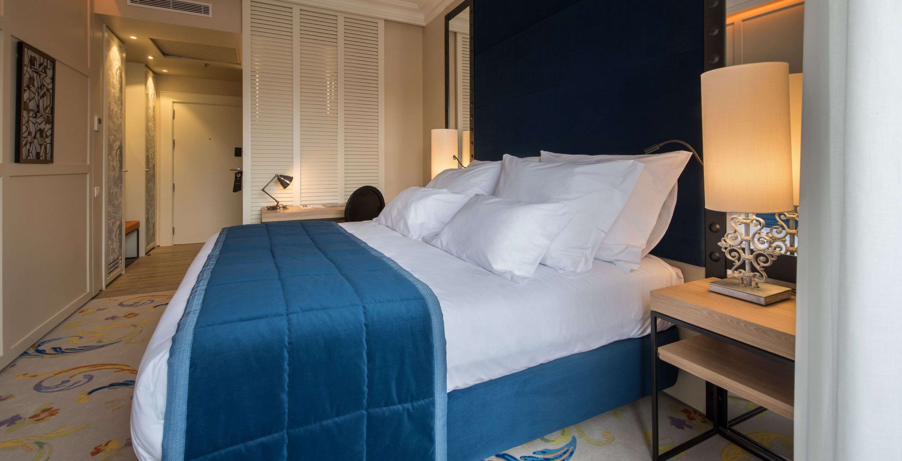 The Superior Plus Room at Pestana Collection Plaza Mayor has a double bed with a blue bedspread and a rug.