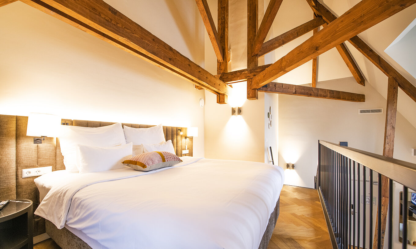 Clock Tower Suite at Pestana Amsterdam Riverside has a double bed, with lamp, and wooden beams on the walls