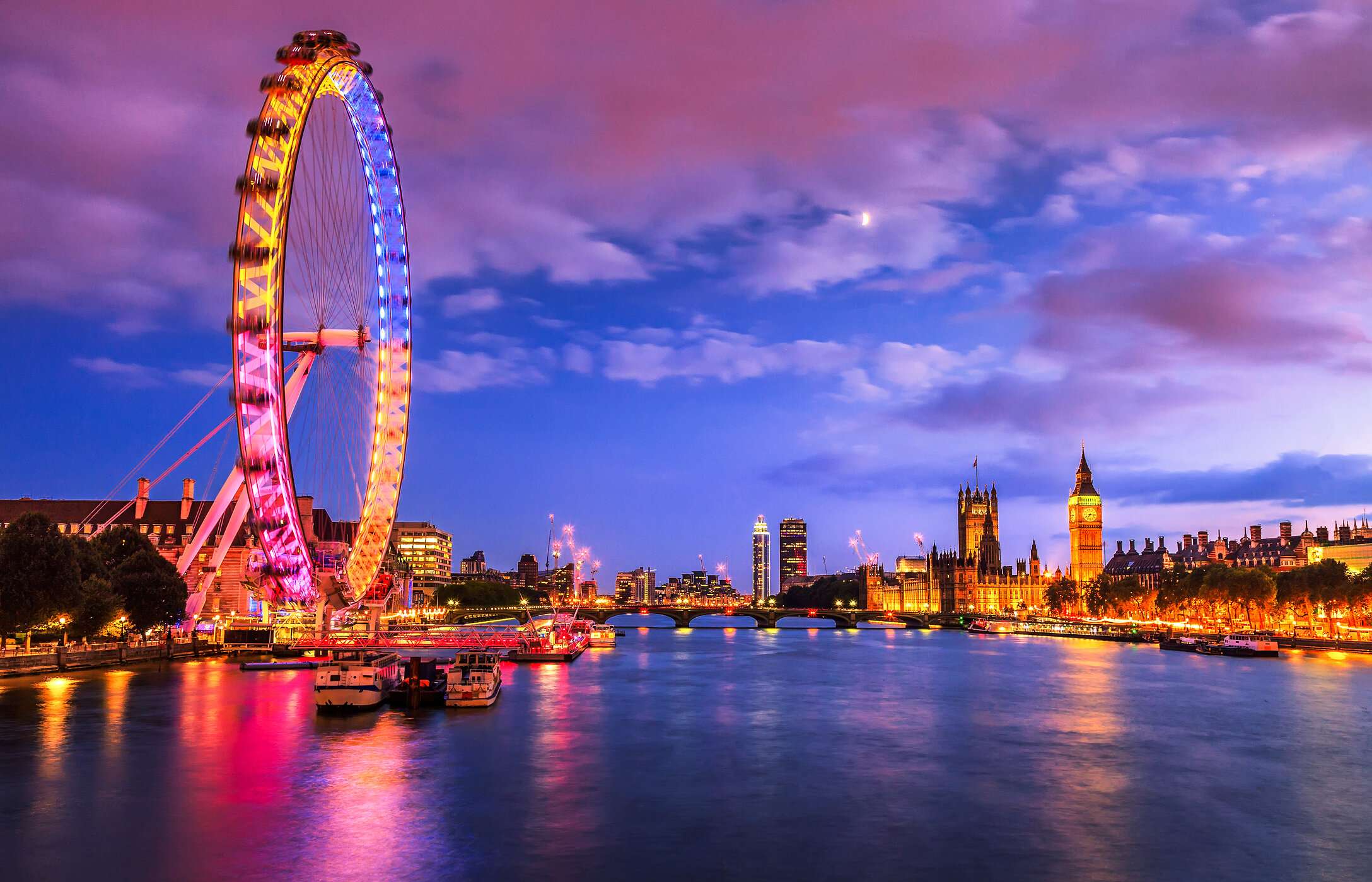 The London Eye Ferris wheel in London, illuminated with vibrant colors by the river, with Big Ben in the background