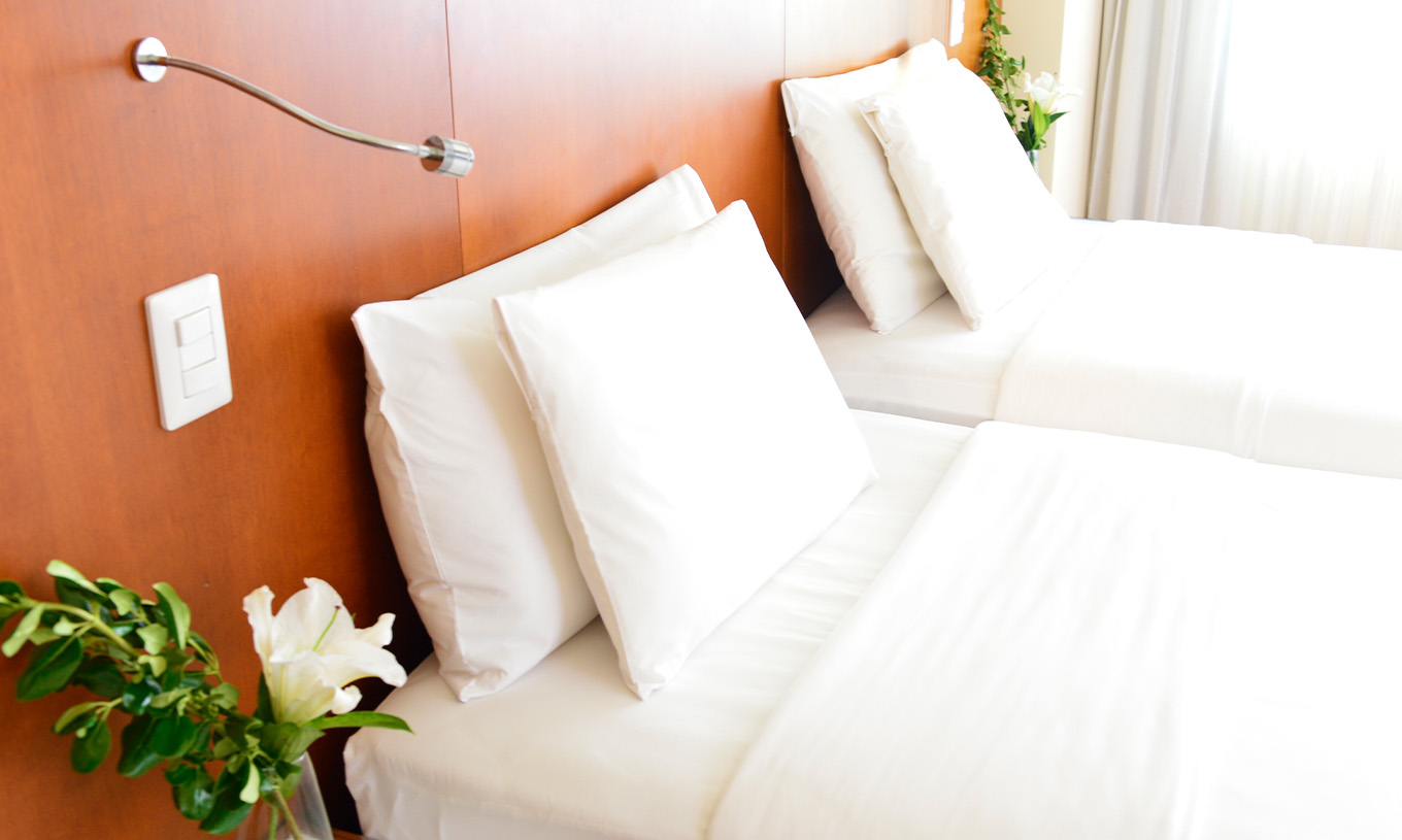 The Twin Executive Room at Pestana Caracas has two beds with white sheets, pillows, and a flower on the bedside table