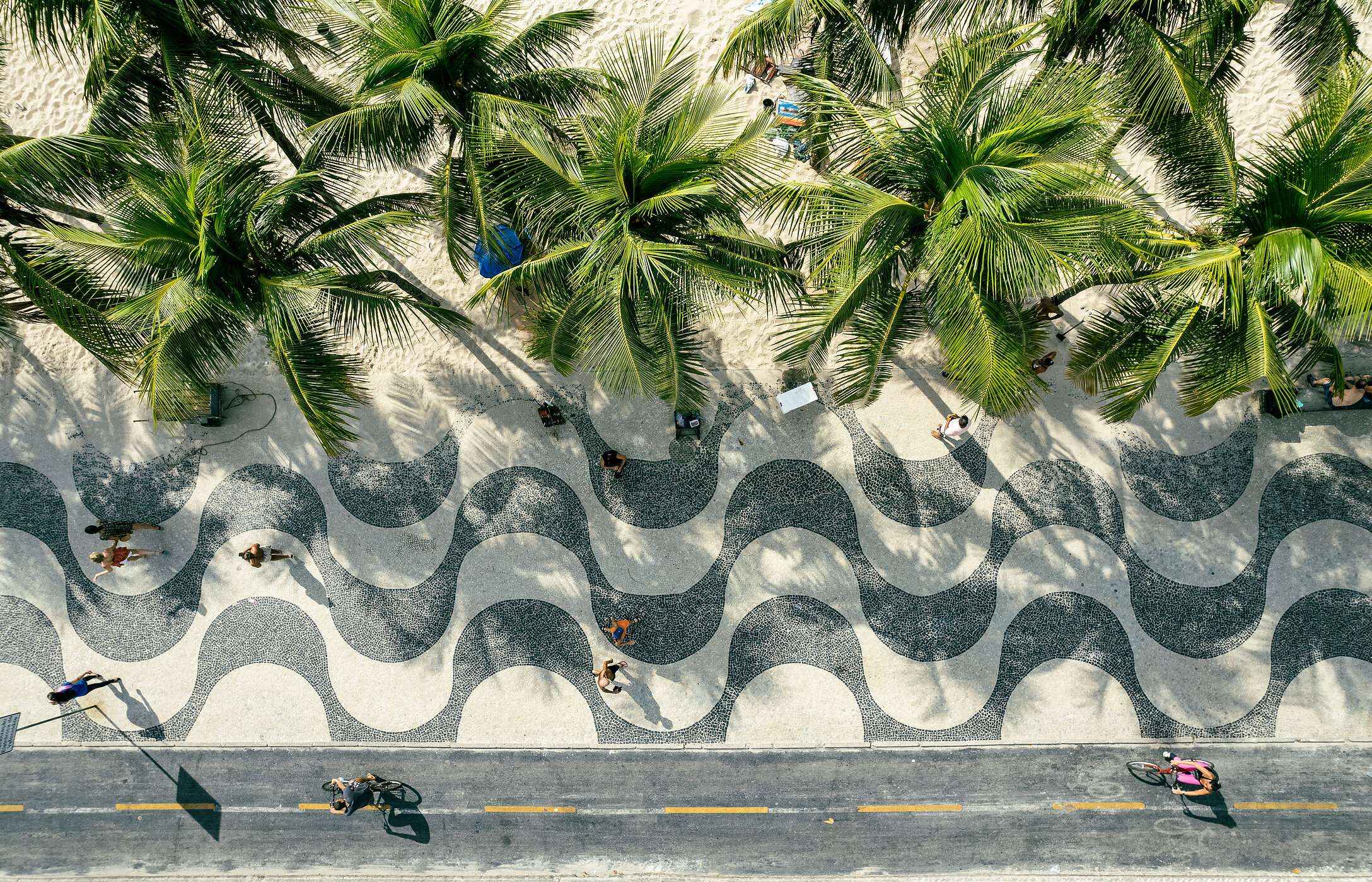 Aerial view of Avenida Atlântica's sidewalk with palm trees and white sand in front of Copacabana Beach in Brazil