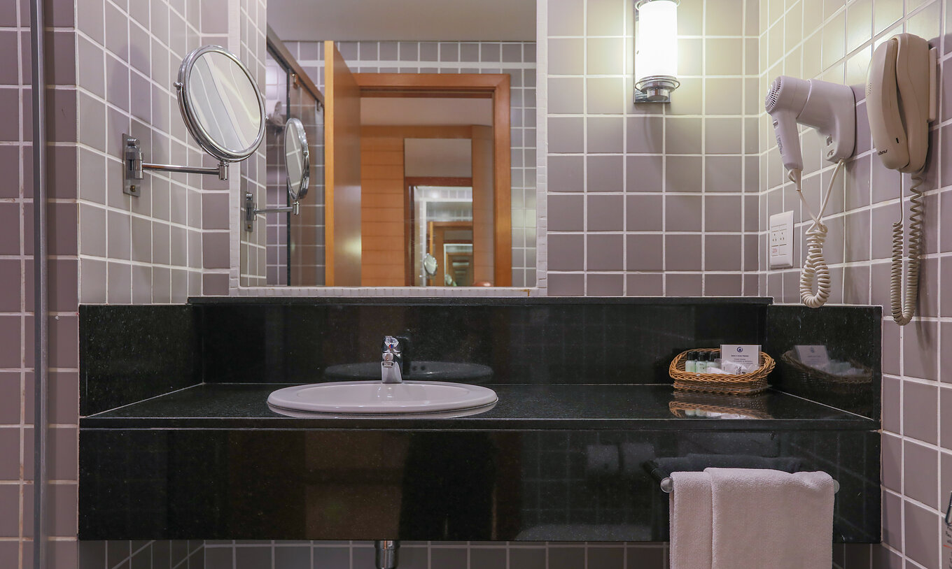The Queen Standard at Pestana Curitiba has a bathroom with gray tiles and a black countertop with a sink