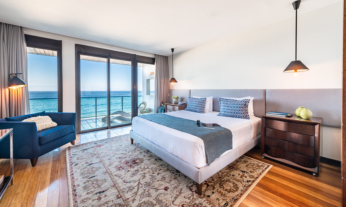 The Presidential Suite of Pestana Rio Atlântica has modern decor, a double bed, armchair, and balcony with sea view