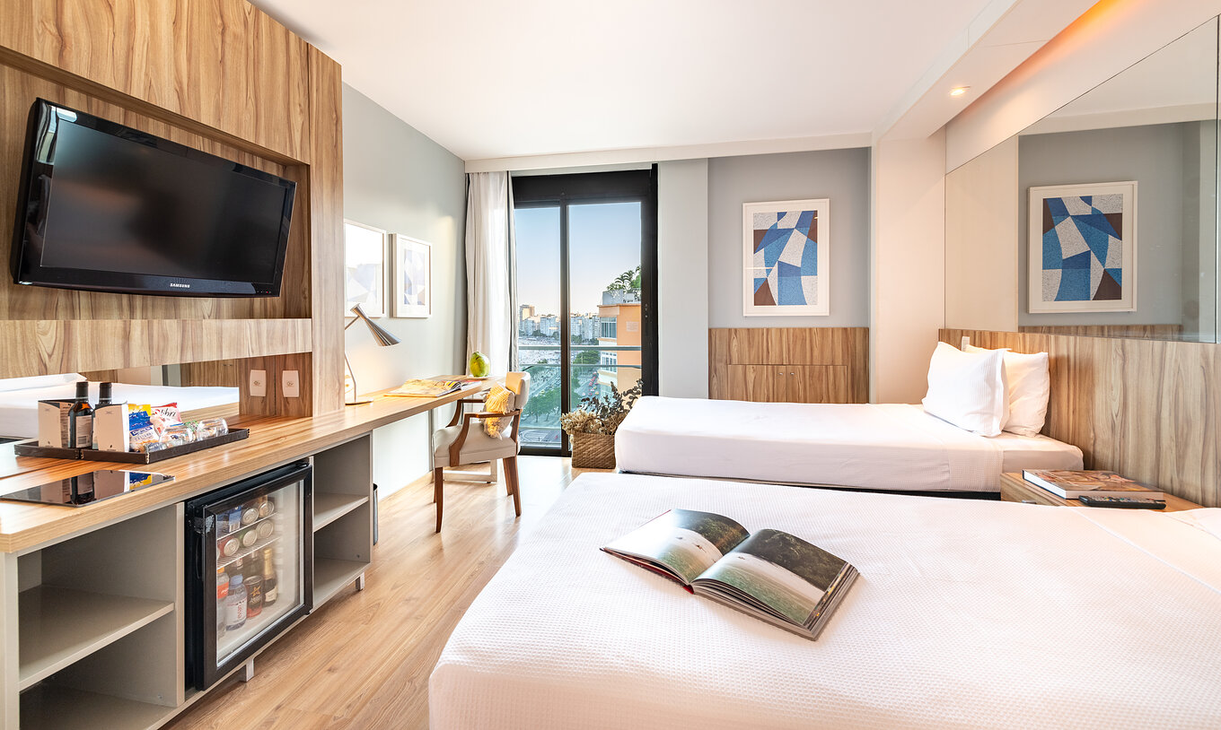 The Queen Side Sea View of Pestana Rio Atlântica has two beds, a television, and a window with a view of Copacabana Beach