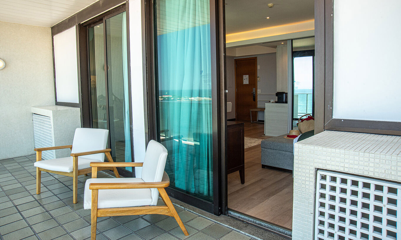 The Suite Beach Front at Pestana Rio Atlântica has a balcony with wooden chairs and room access.