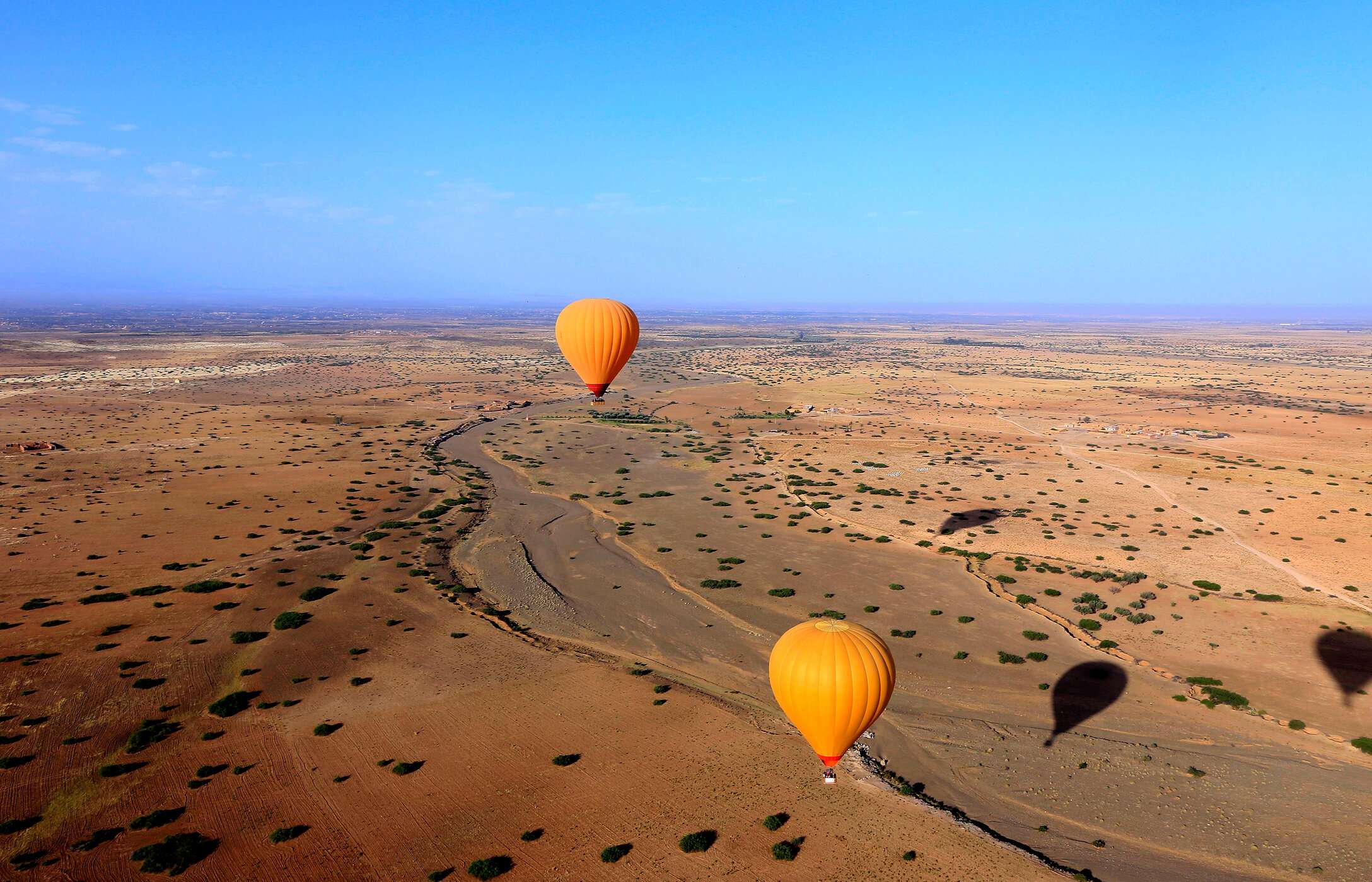 Aerial view of a plain near Marrakech, with two orange hot air balloons flying over the plain