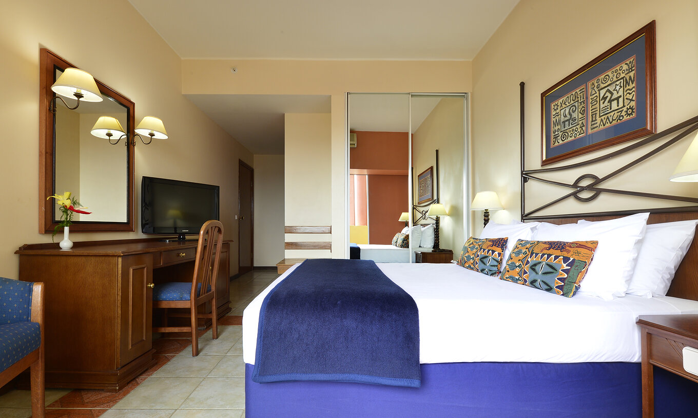 The Standard Double of Pestana Rovuma has a double bed, a wardrobe with mirror, a desk, and a television
