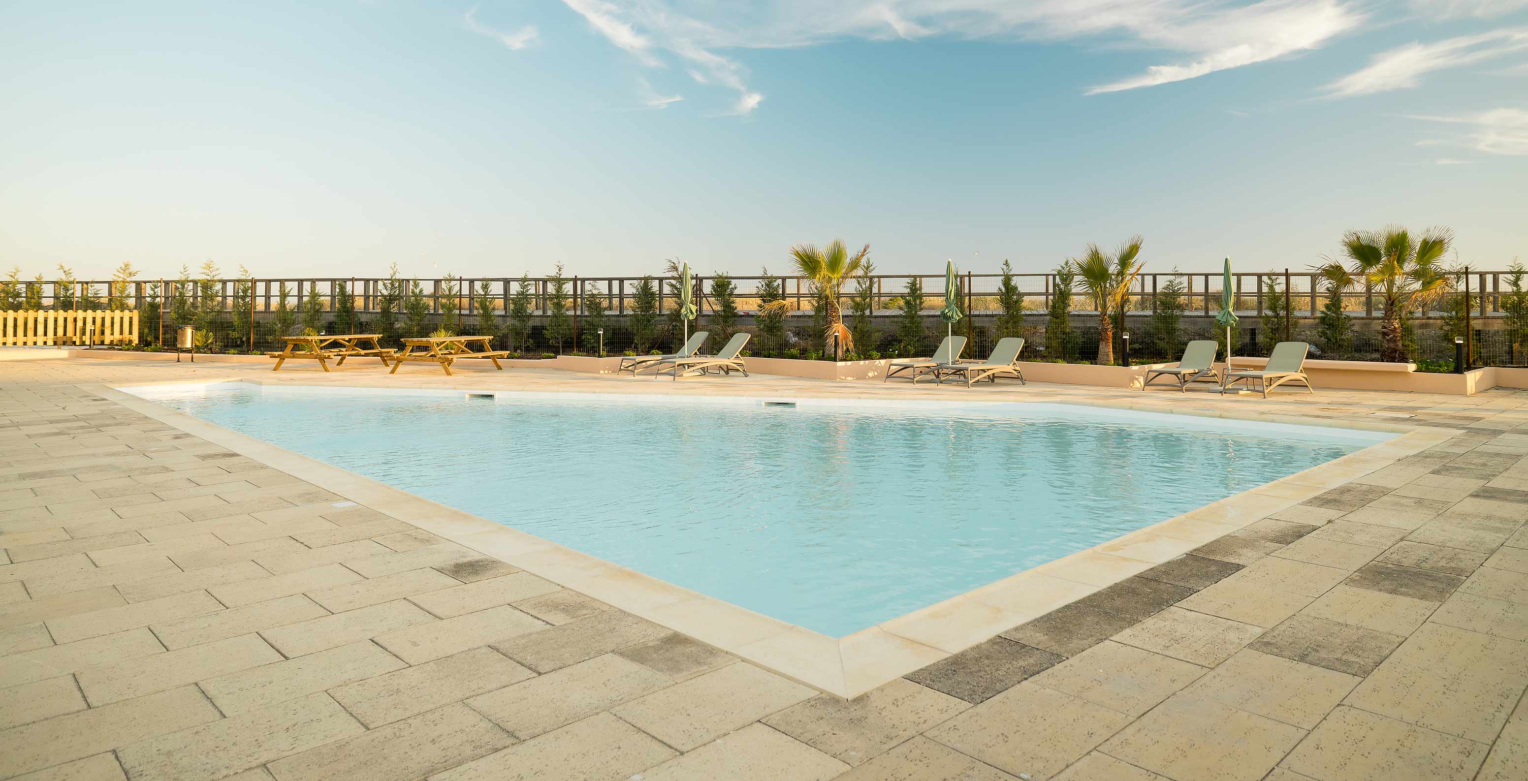 Kids’ pool at beach hotel, several sun loungers, palm trees, garden area and view of the path leading to the beach