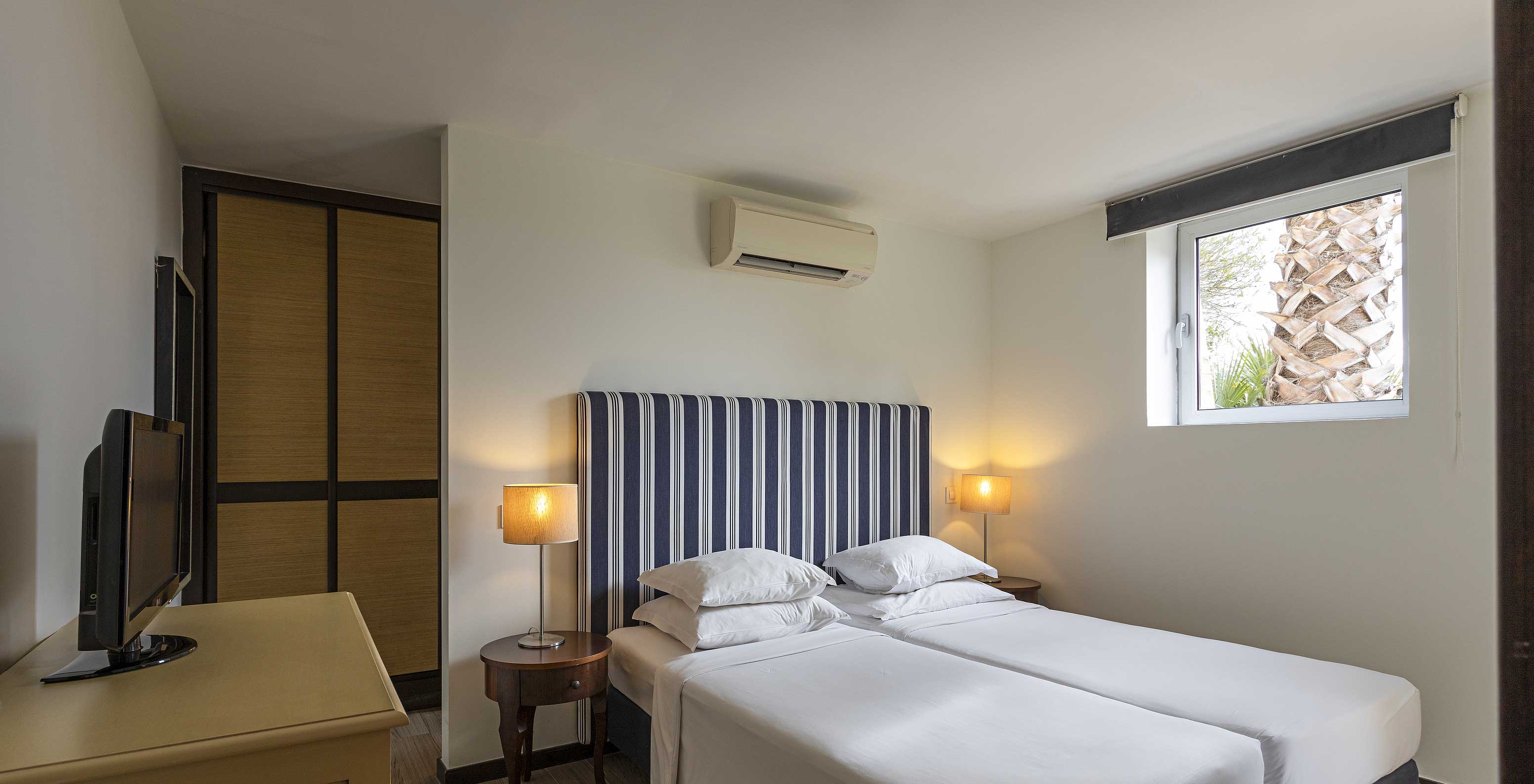 The Cliff Suite T2 at Pestana Alvor Praia has a bedroom with a bed, a television, a wardrobe, and air conditioning