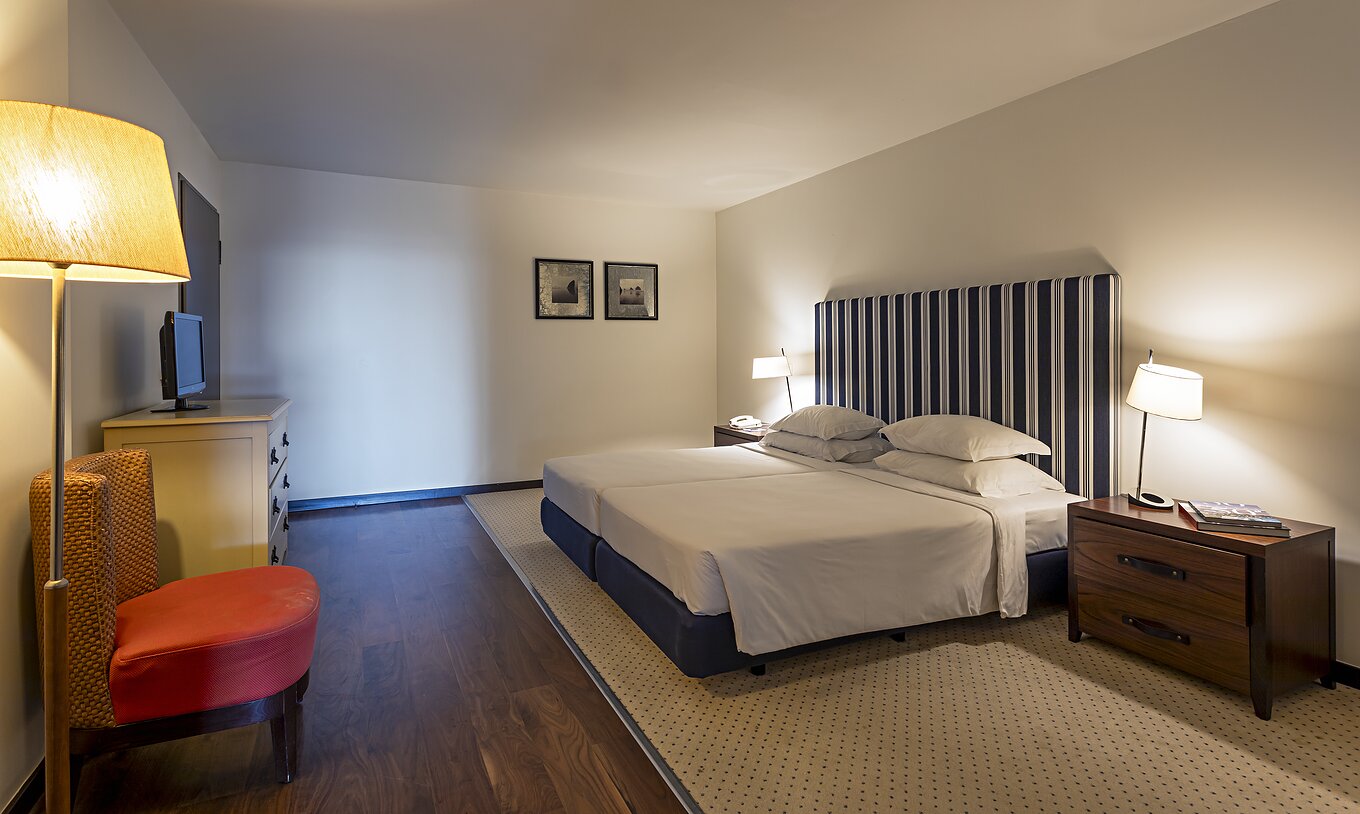 The Cliff Suite T2 at Pestana Alvor Praia has a large bedroom with a double bed, two paintings, and a dresser with a TV