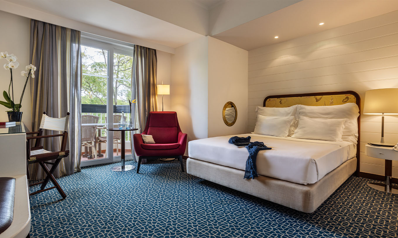 The Garden View Suite at Pestana Alvor Praia has a double bed, a red armchair, and a view with chairs