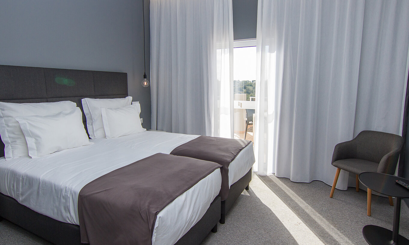 The Classic Pool View room at Pestana Gramacho Residences features two single beds, a chair, and a window