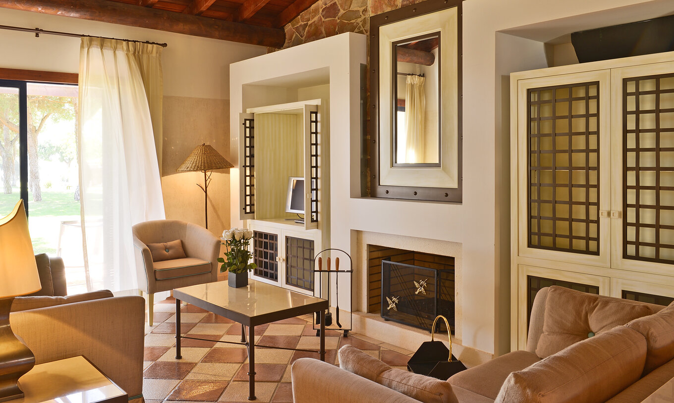 The Garden View Suite at Pestana Vila Sol - Vilamoura has a living room with sofas, a coffee table, a fireplace, and a window