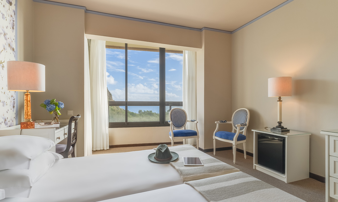 Standard Garden View room at Pestana Bahia Praia has two chairs near the window with a view of the green island landscape
