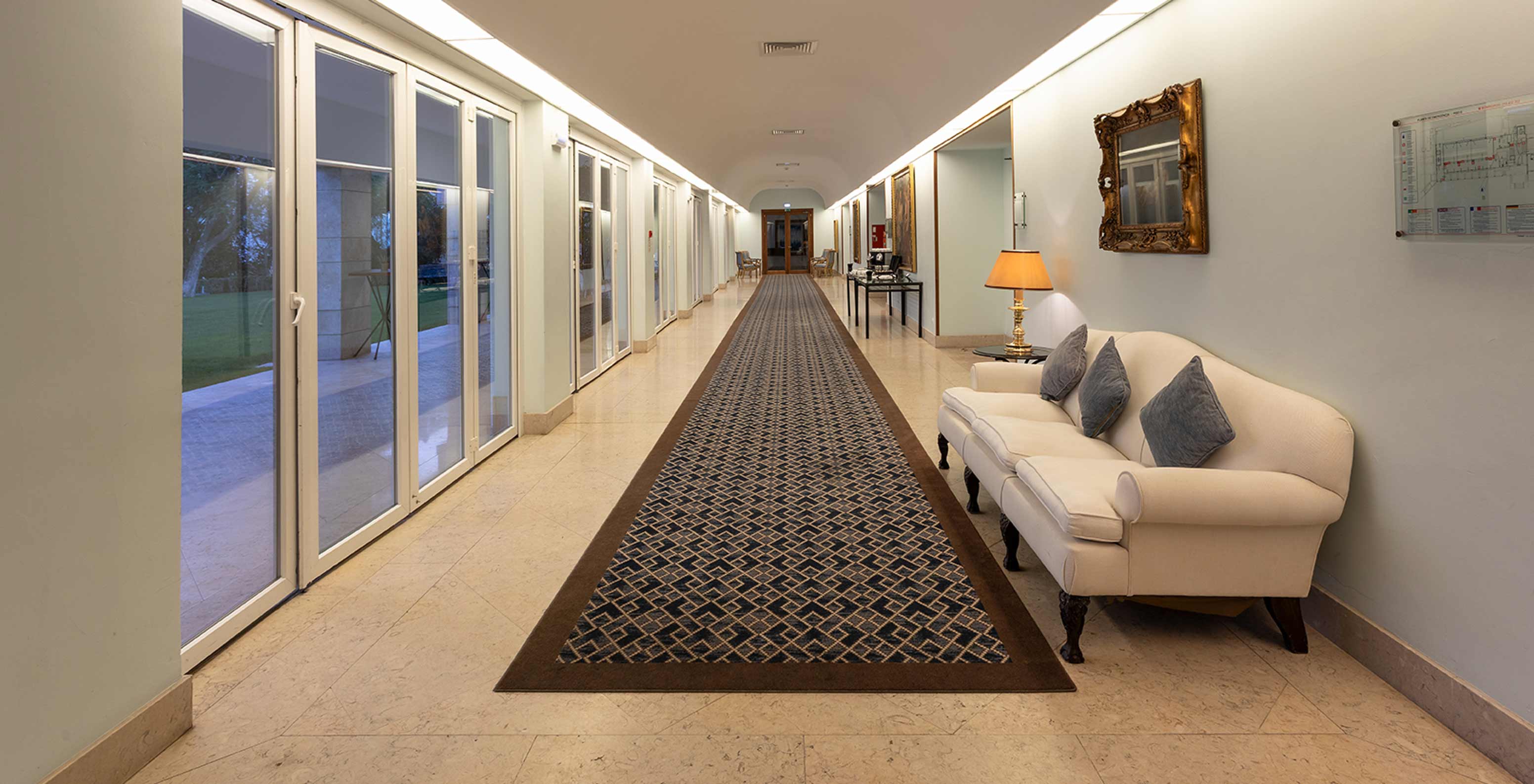 Pestana Palace Lisboa has a foyer with a long blue carpet, a sofa and large windows with long curtains