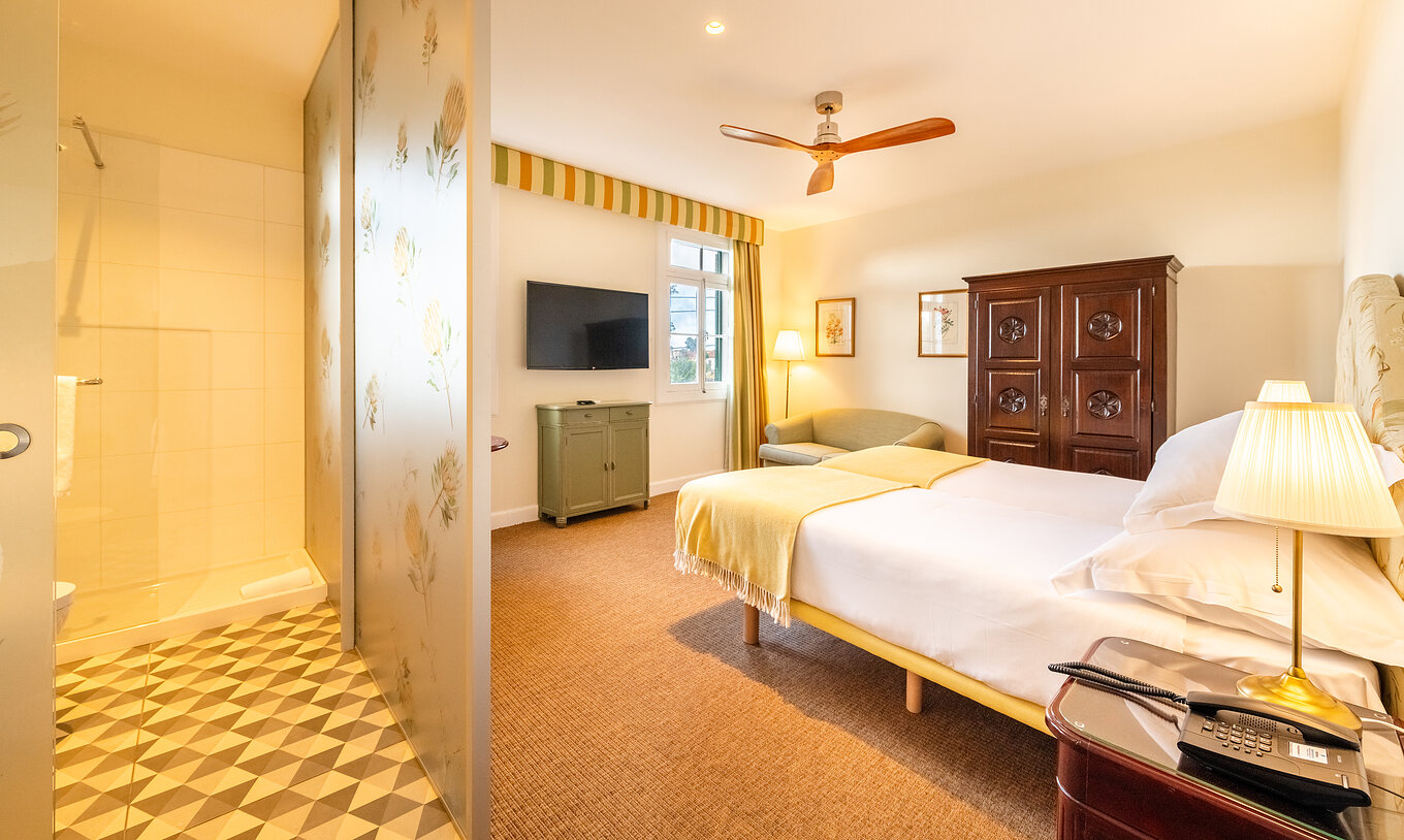 The Manor House - 1 of Pestana Quinta do Arco has two beds, wooden wardrobe, fan, and divider with the bathroom