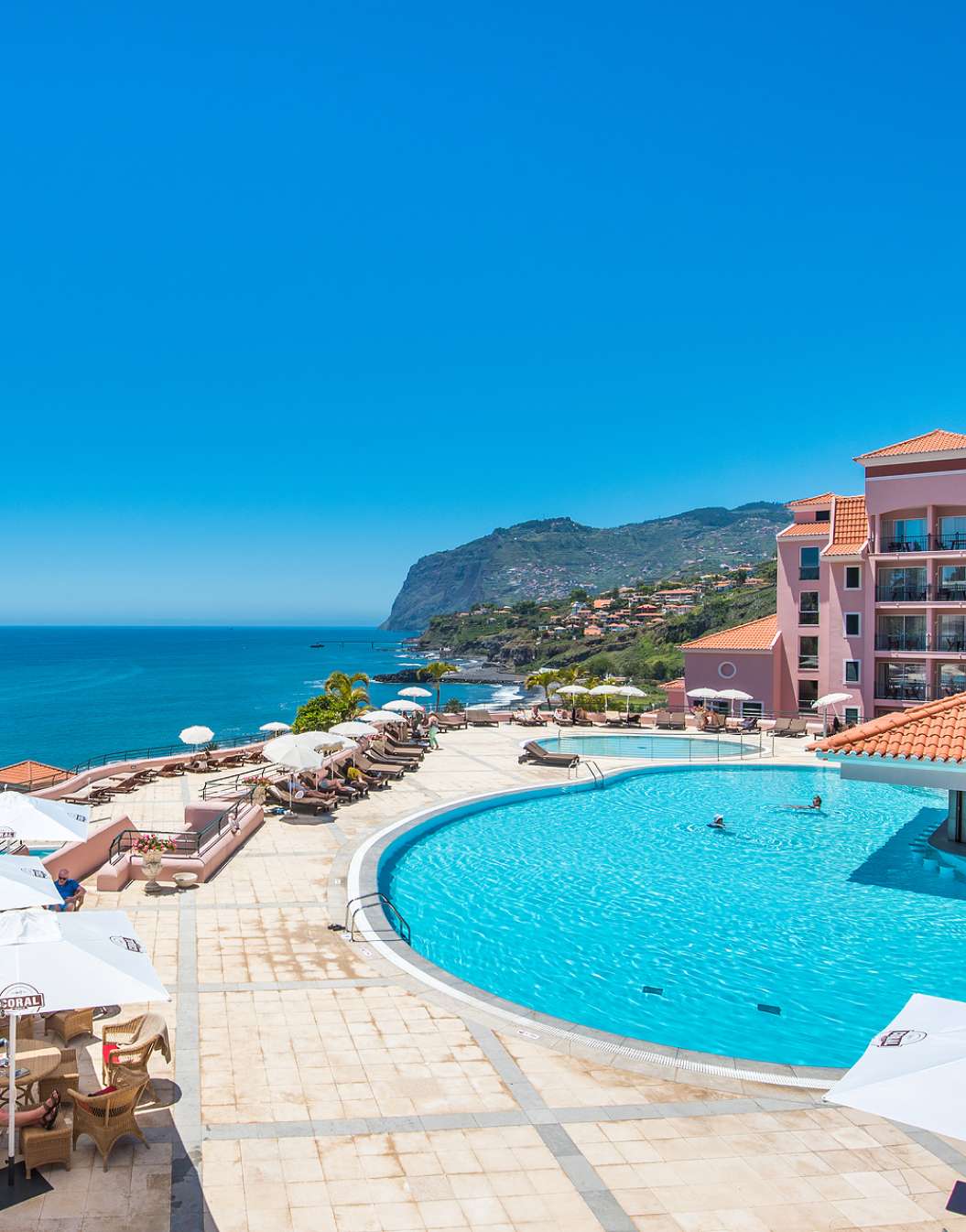 Exterior view of the outdoor pool of Pestana Royal All Inclusive, with the ocean in the background on a clear sky day