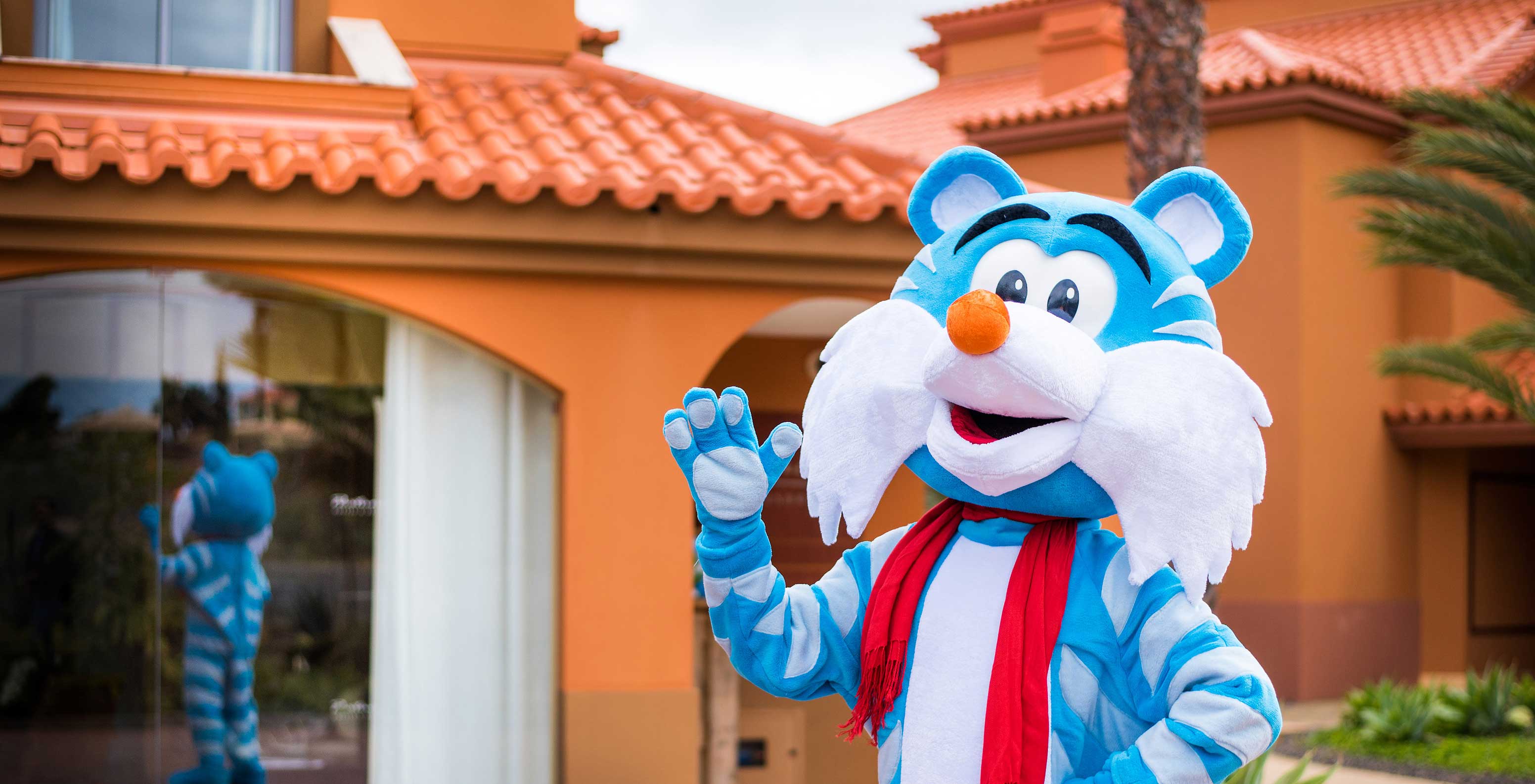 Blue & white tiger mascot waving at Pestana Porto Santo, reflection in window