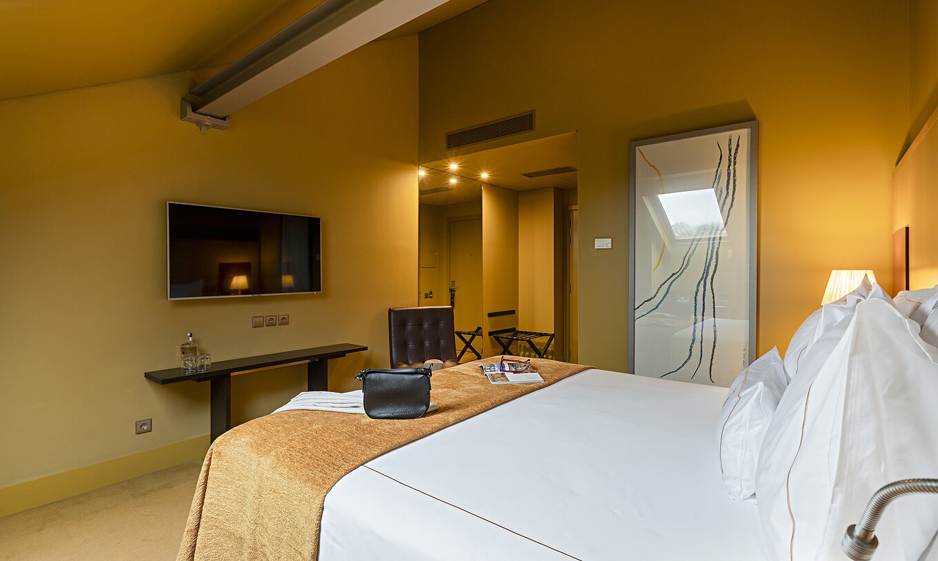 Pestana Palácio do Freixo’s Classic Attic has a double bed, TV in front, and a table with water