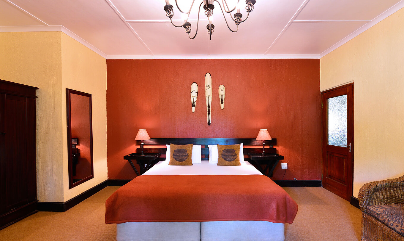 The Rhino Family Cottage at Pestana Kruger Lodge has a double bed and typical African decor in red tones