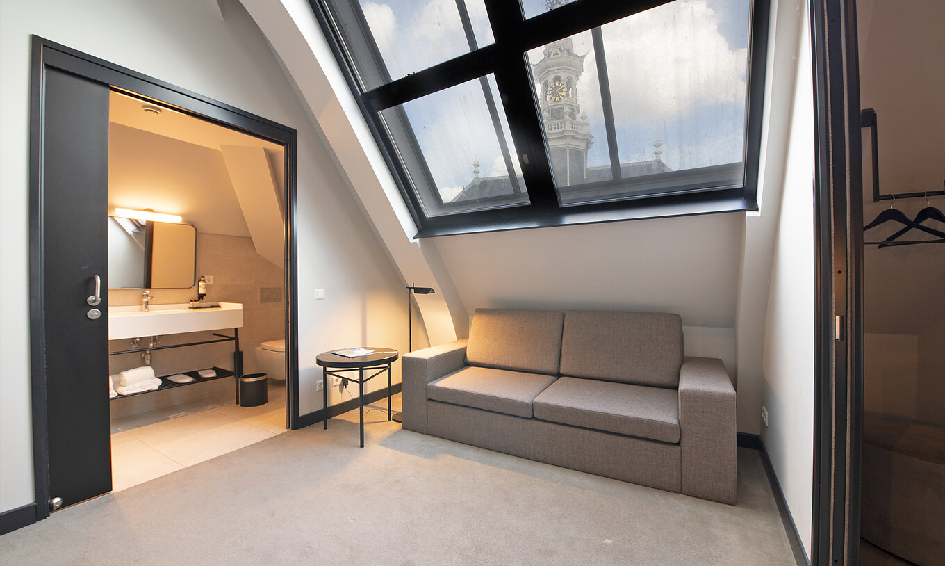 Loft room at Pestana Amsterdam Riverside has a gray sofa, and a bathroom with sink and mirror