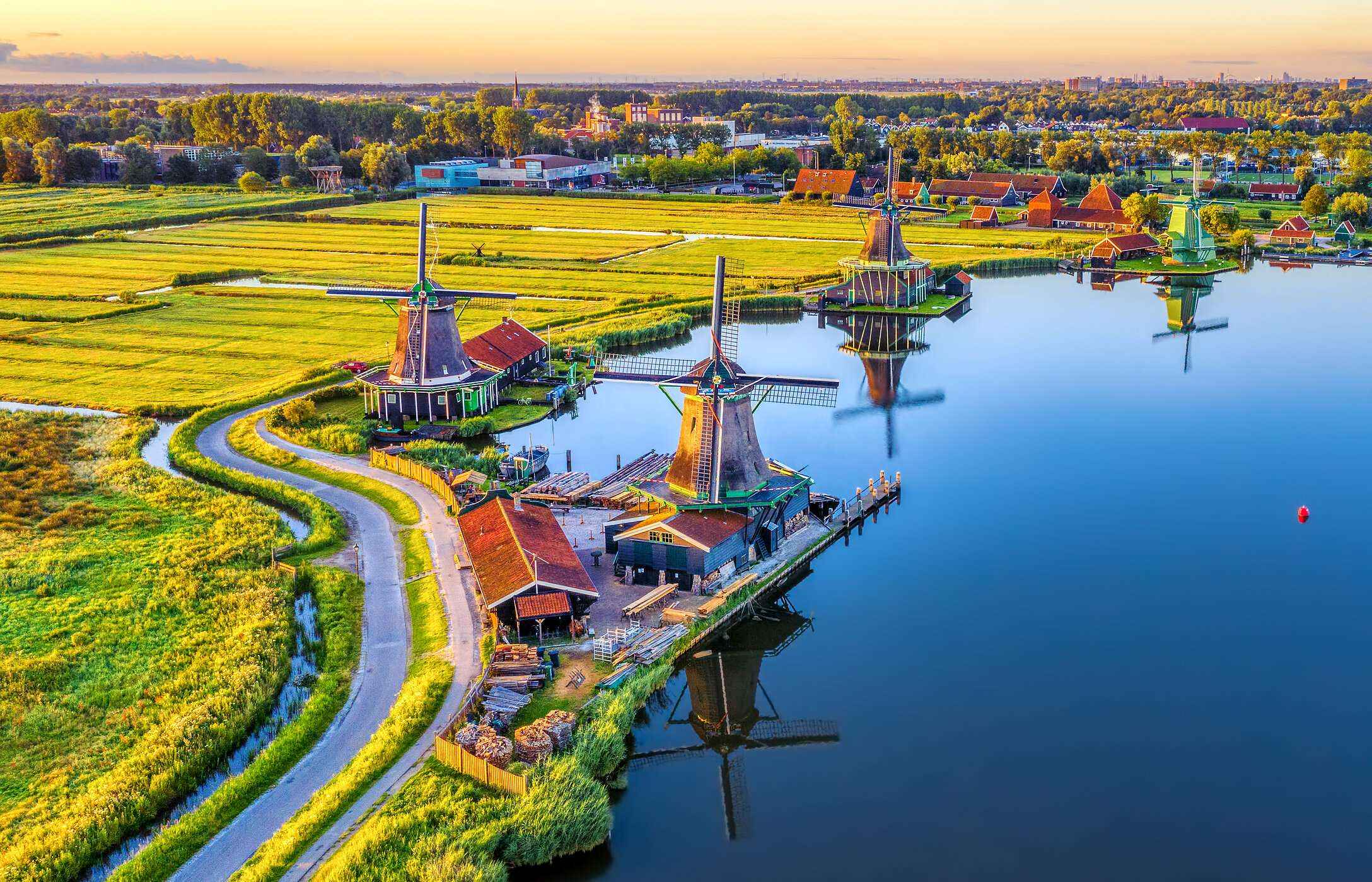 Aerial view of Zaandam, with its typical windmills by a lake, surrounded by green fields.