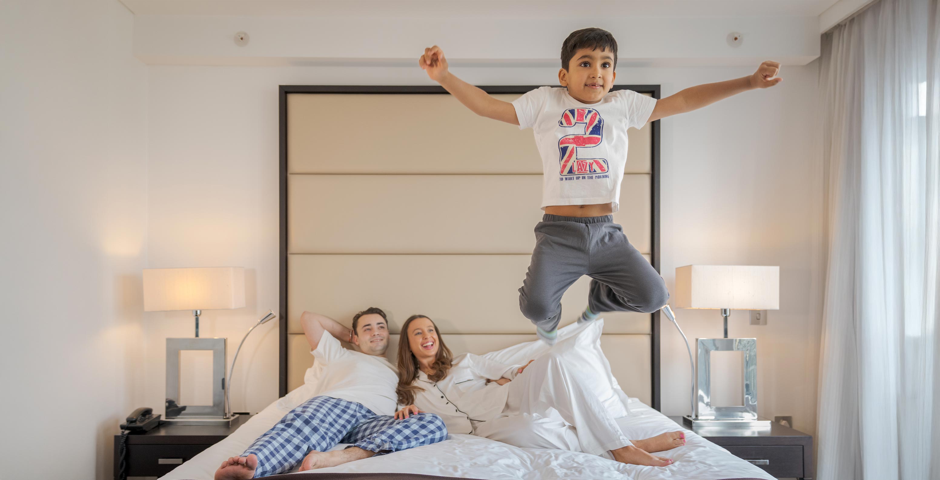 The Deluxe Family at Pestana Chelsea Bridge has a double bed with a family lying down and a child jumping