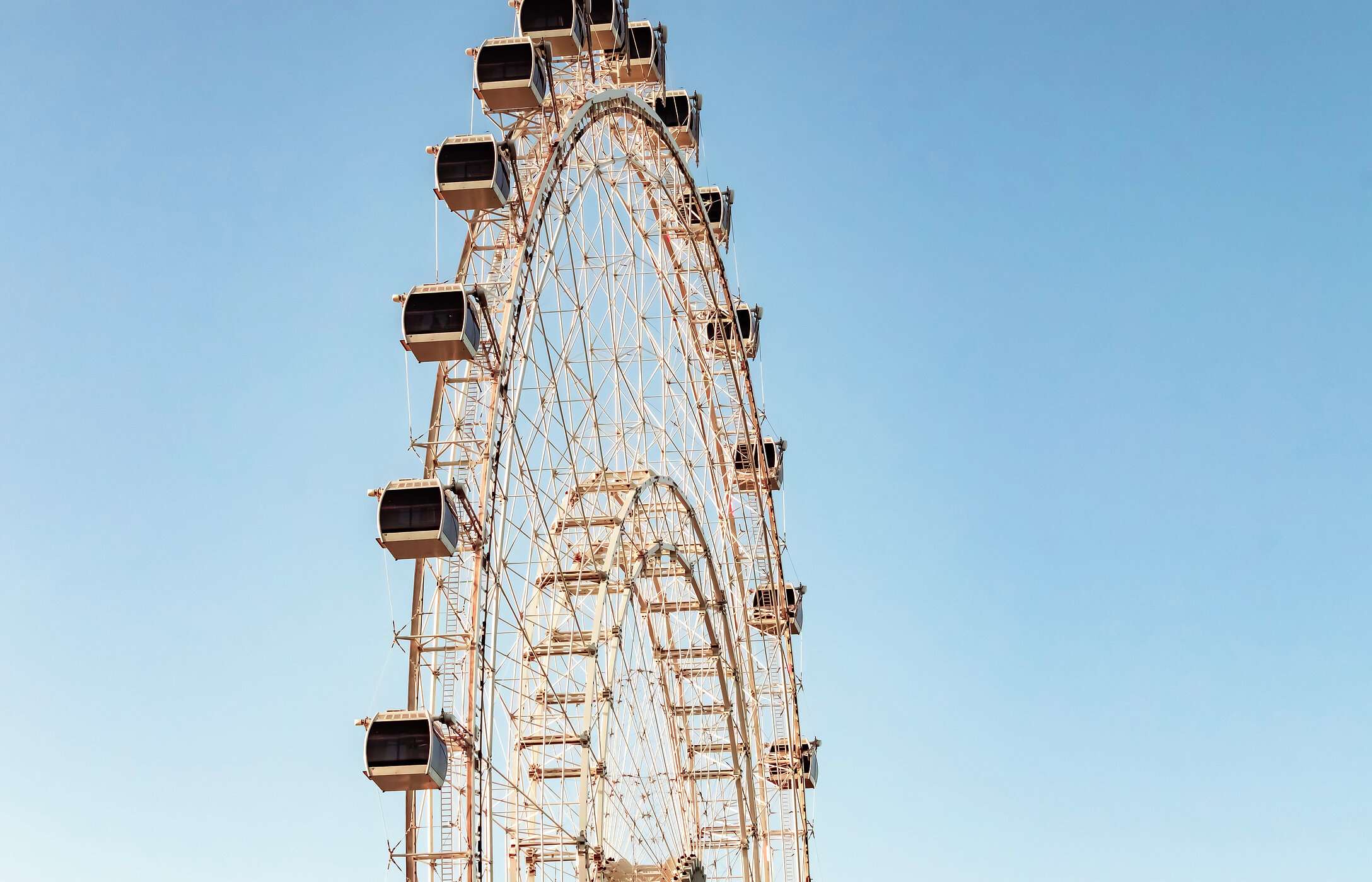 View of a Ferris wheel with white cabins and a clear blue sky in the background