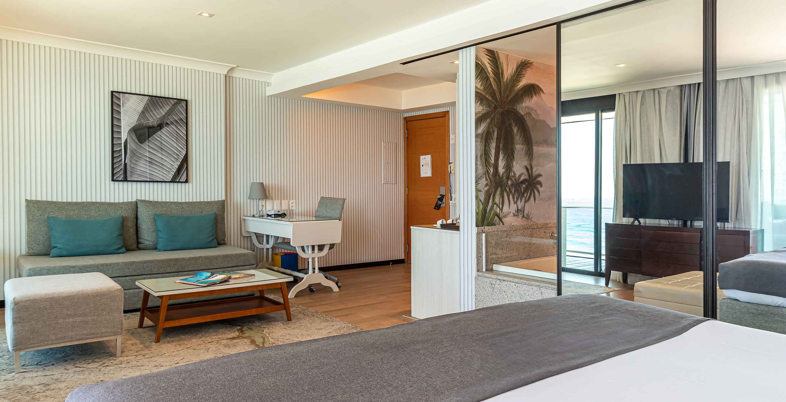 La Suite Frente al Mar del Pestana Rio Atlântica tiene cuarto moderno con cama, sofá, mesa y TV.