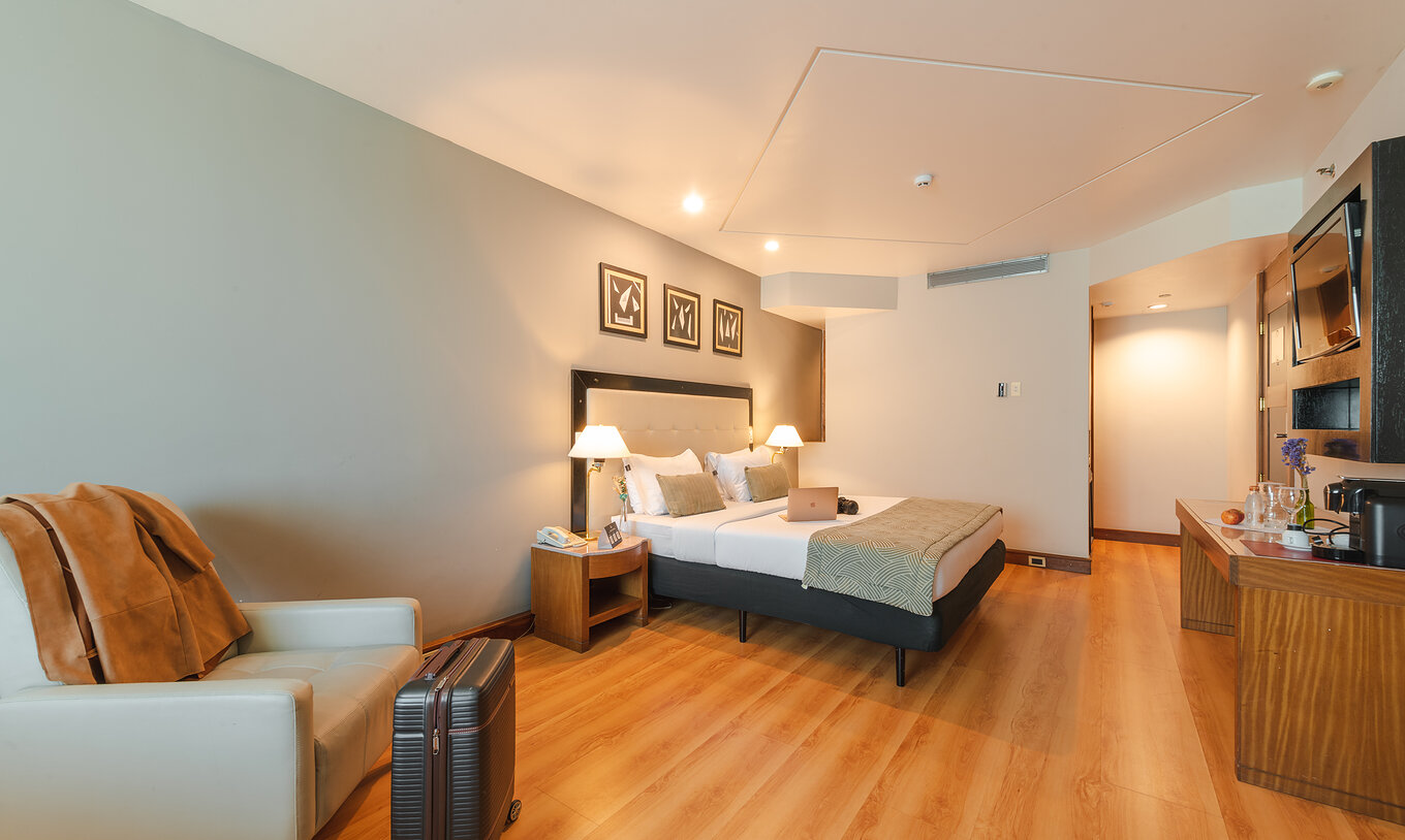 La Suite Ejecutiva del Pestana São Paulo tiene un cuarto con cama de matrimonio, sillón y una maleta