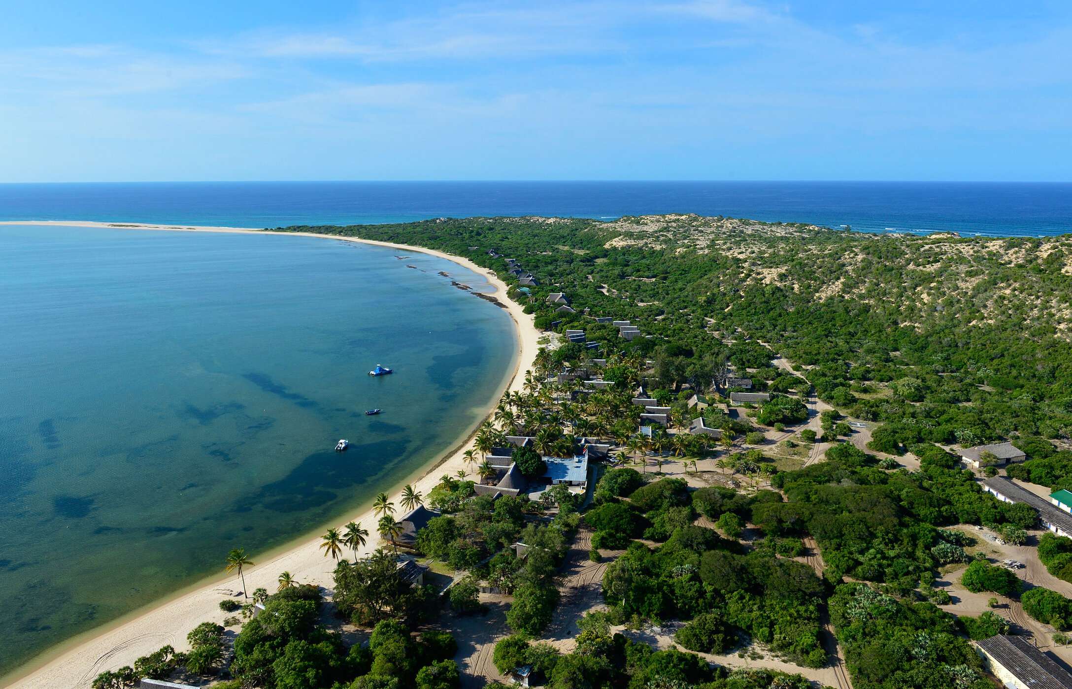 Vista aérea de la isla de Bazaruto en Mozambique, con una playa de arena blanca, rodeada de vegetación y algunos edificios.