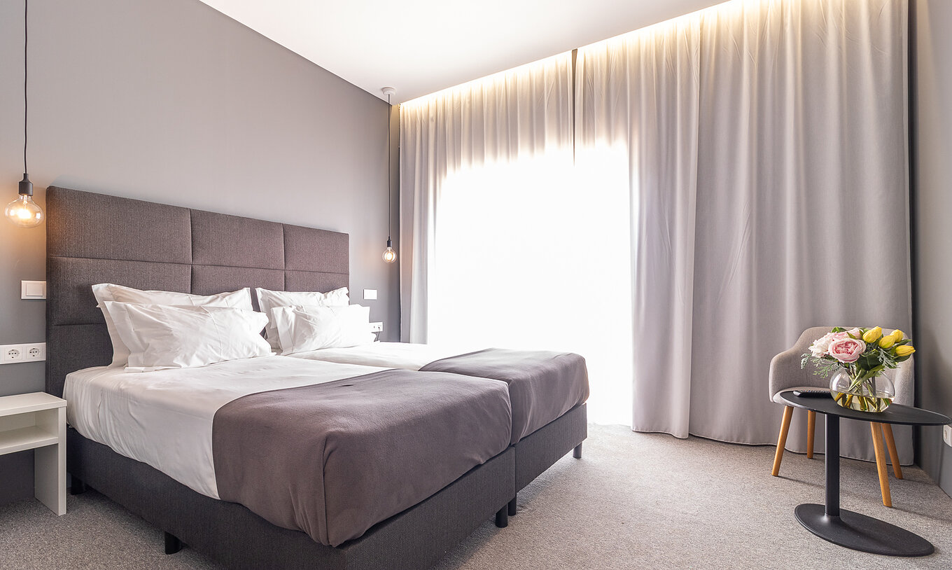 Habitación Clásica en Pestana Gramacho Residences con dos camas, cortinas y mesa con flores
