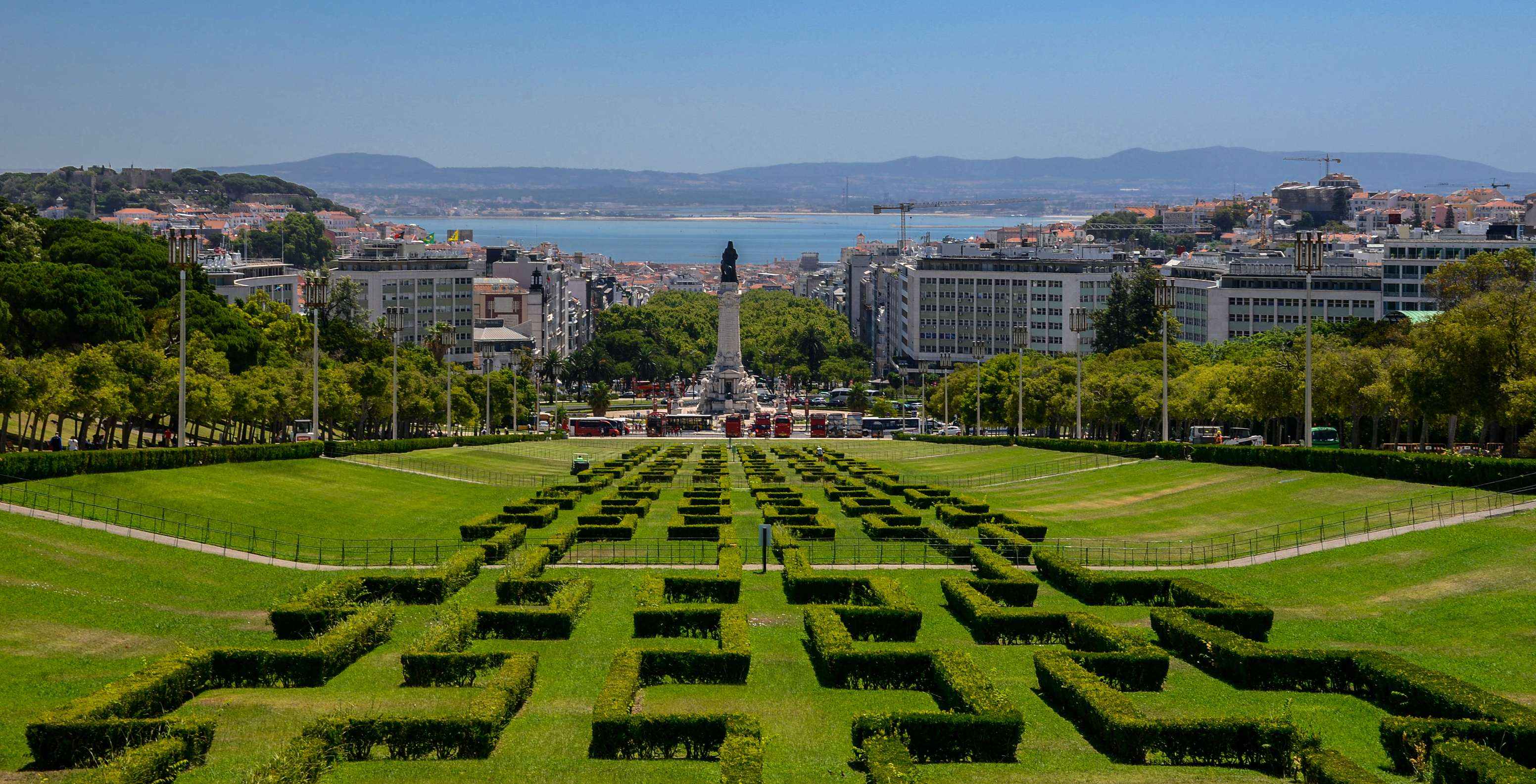 Vista aérea del Parque Eduardo VII, con jardines verdes, edificios, la estatua del Marqués de Pombal y el Río Tajo