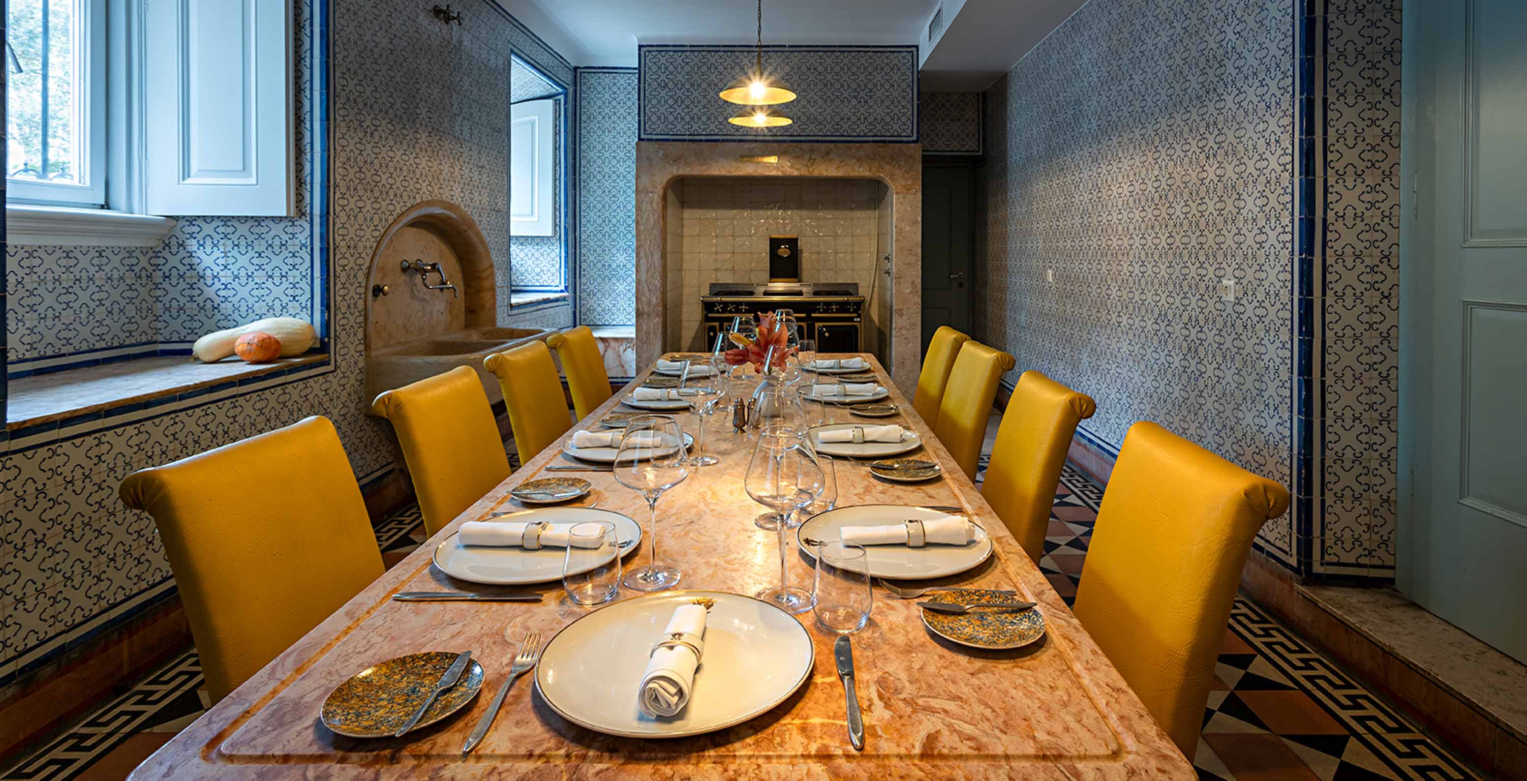El Pestana Palace Lisboa tiene una cocina antigua para eventos privados, con una mesa de piedra y sillas amarillas