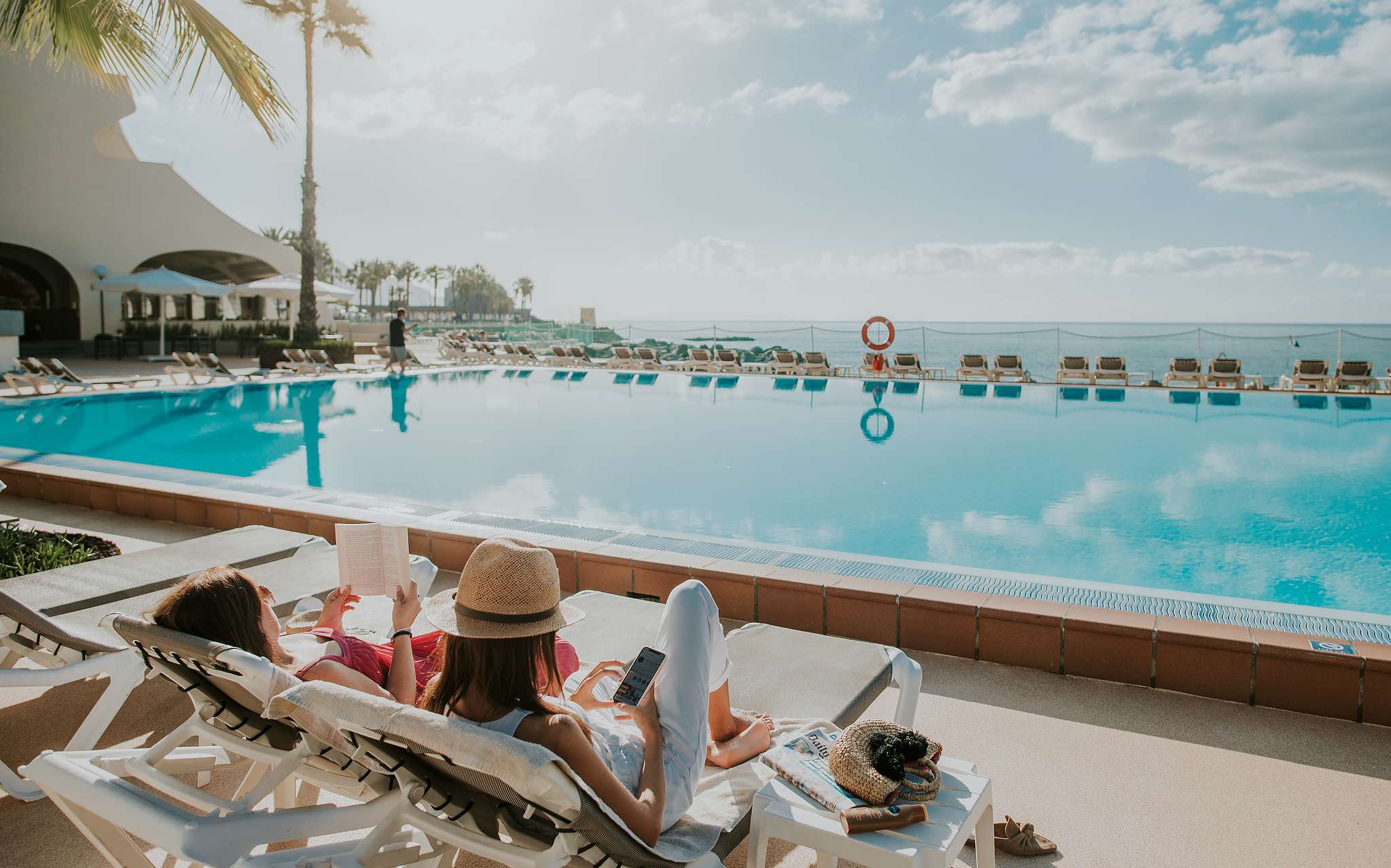 Piscina de Pestana Madeira Beach Club, con vista al océano y dos mujeres relajándose en las tumbonas