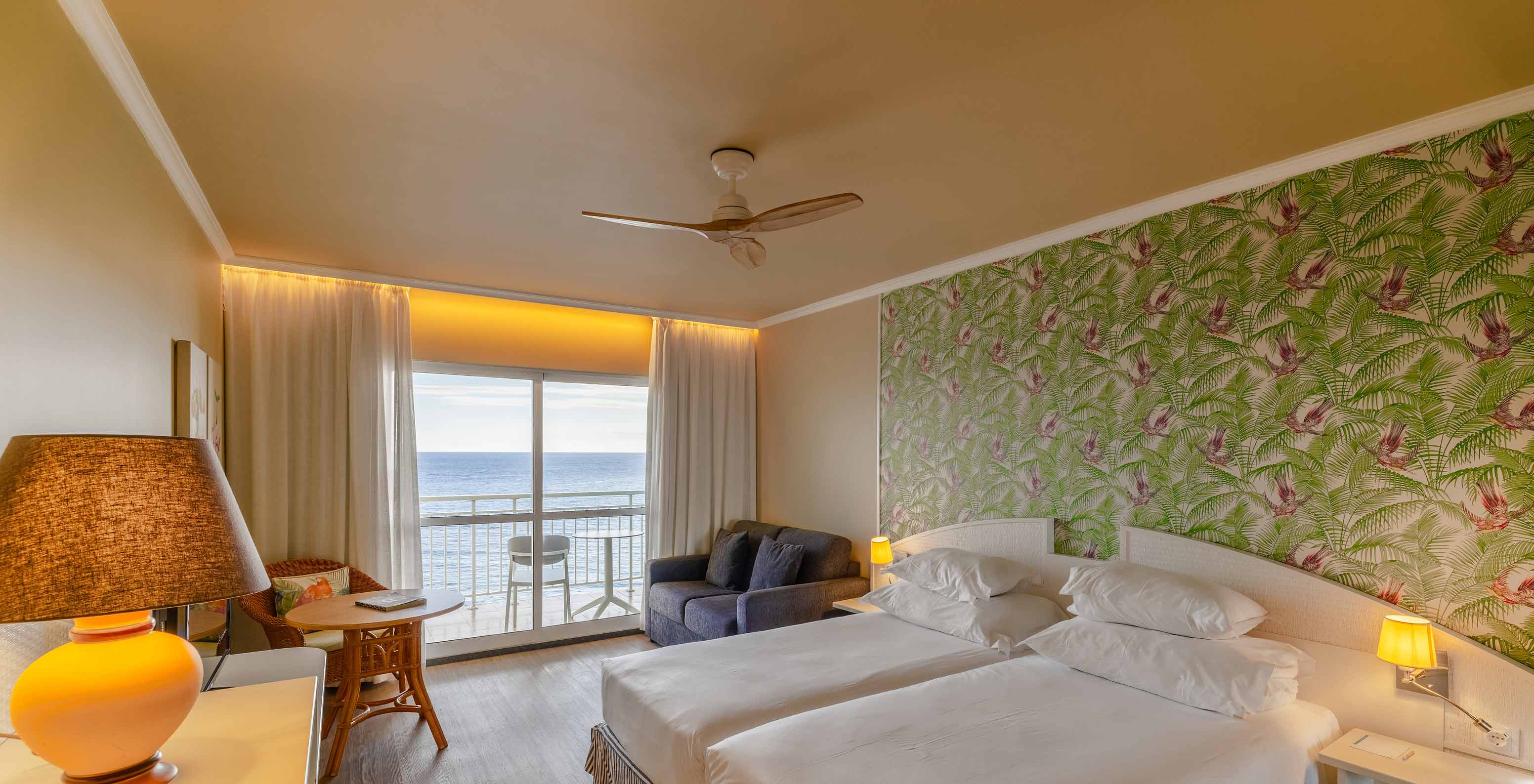 El Premium Sea View del Pestana Ocean Bay All Inclusive tiene una cama doble, papel pintado con palmeras, un sofá y balcón