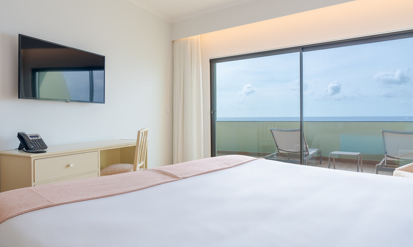 La Suite Superior Vista Mar del Pestana Vila Lido Madeira tiene una cama de casal con televisión y escritorio al frente