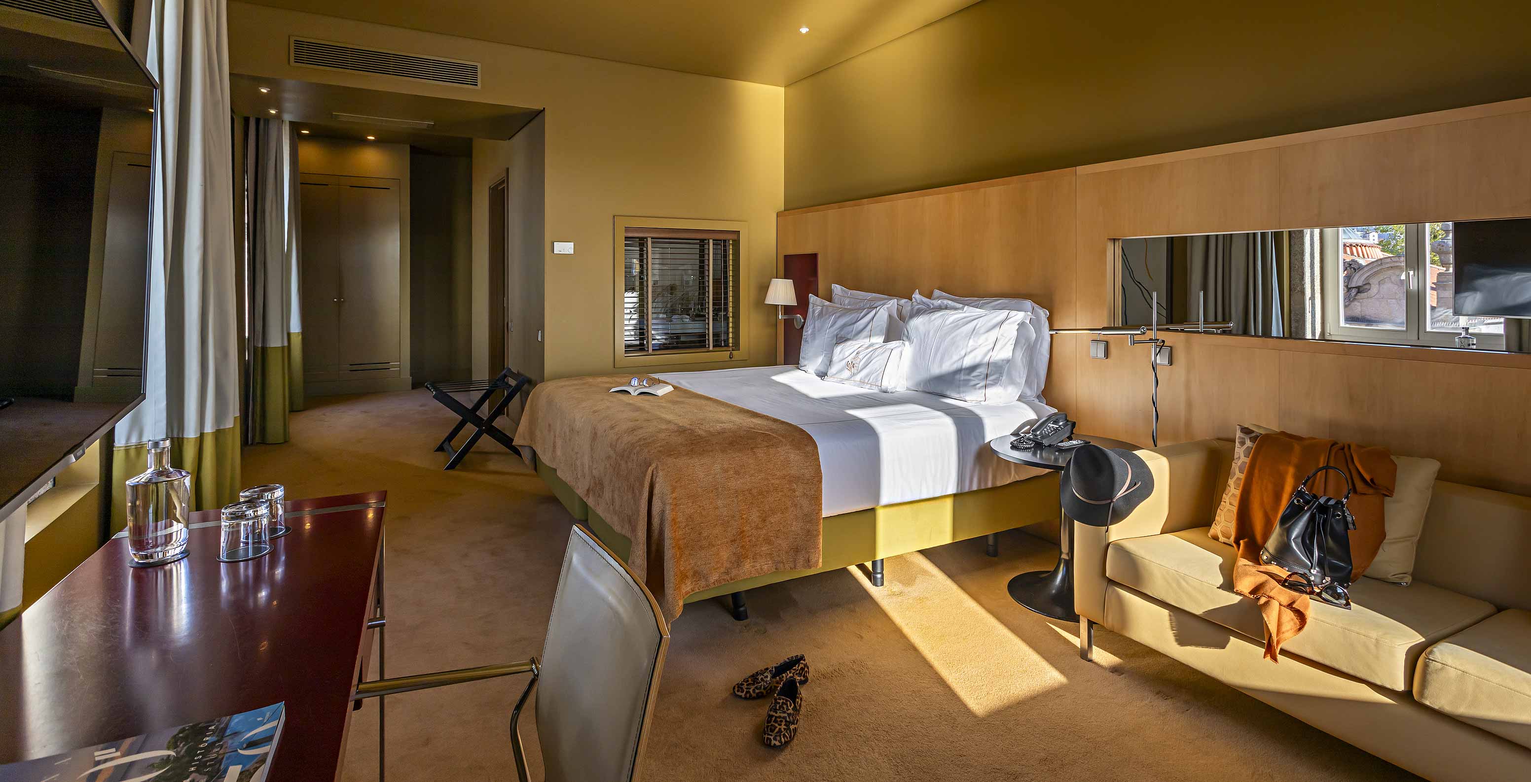 El Deluxe Grand View tiene una cama doble con una manta color camel, un sofá y un escritorio