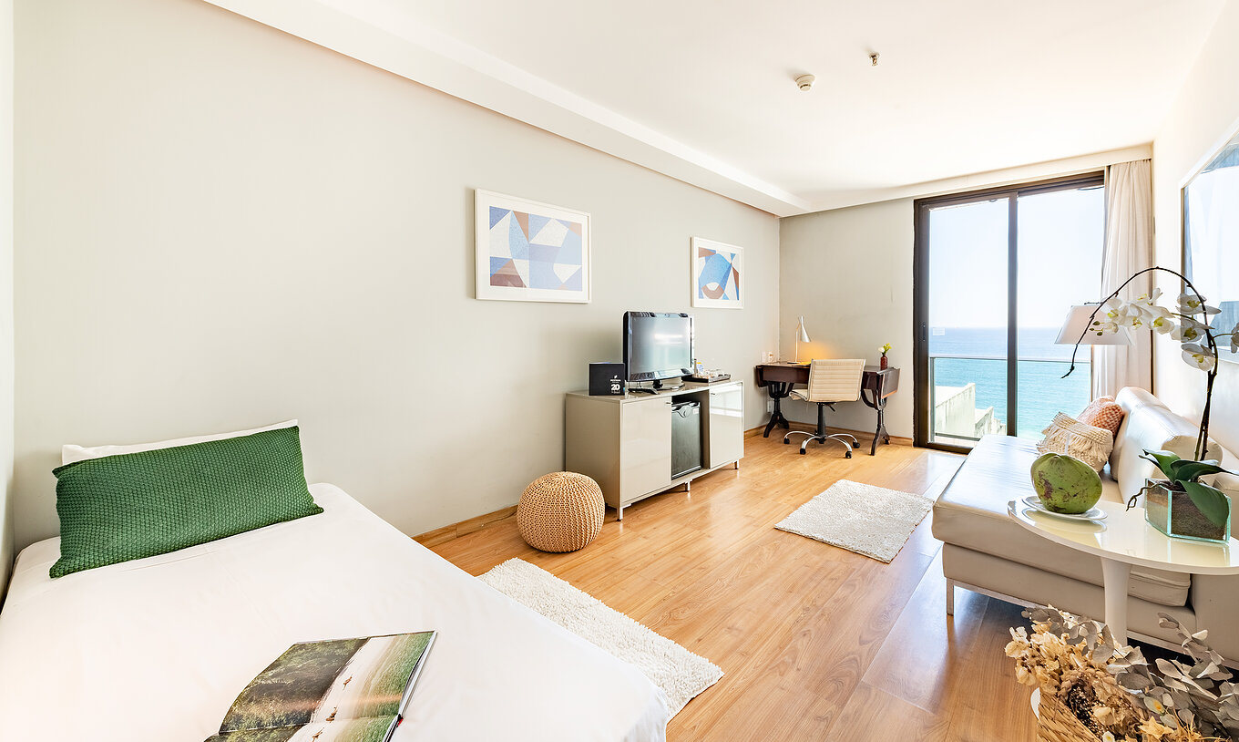 La Suite Con Vista Lateral al Mar del Pestana Rio Atlântica tiene una sala con sofá, televisión y ventana con vista al mar