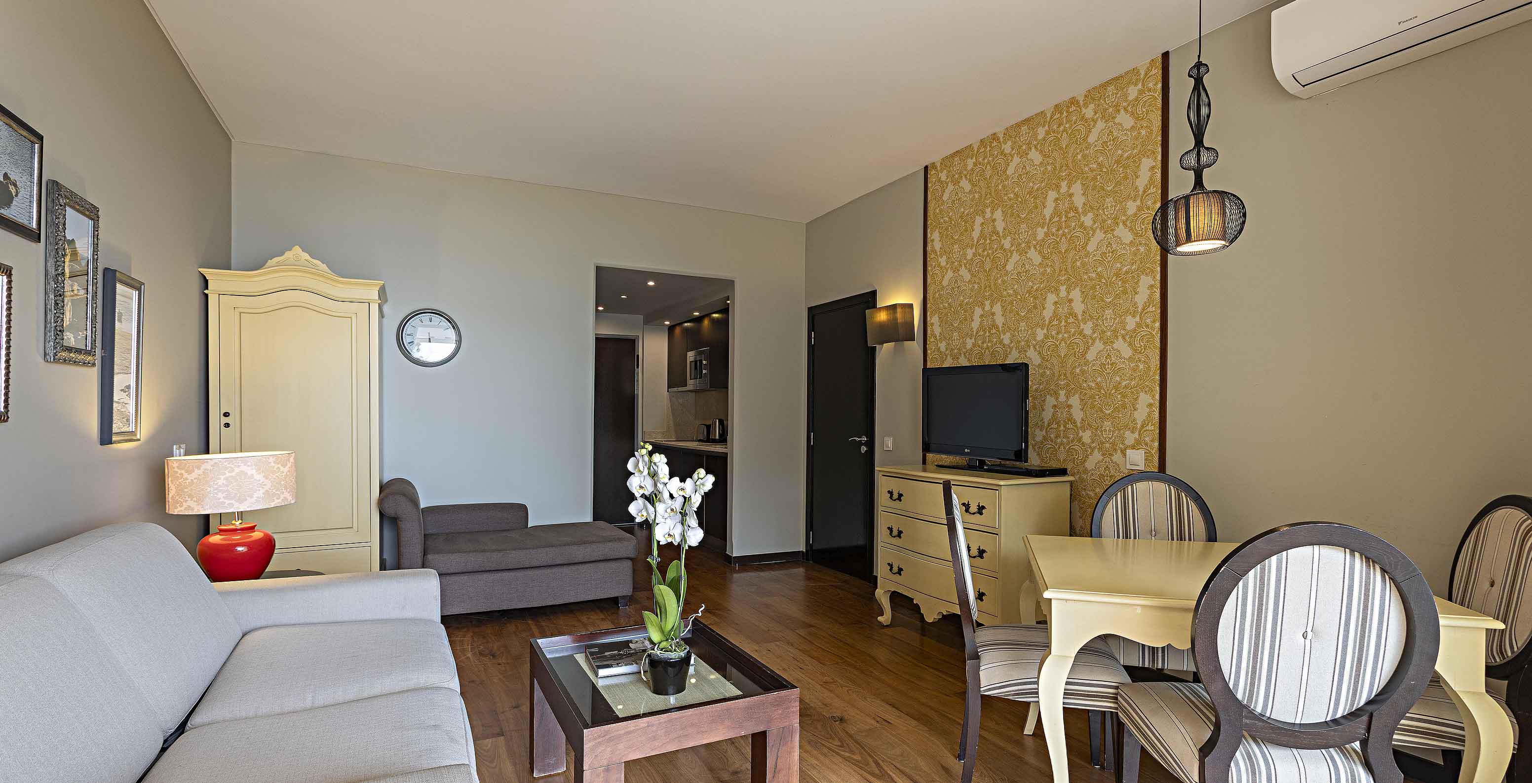 La Suite Cliff T1 en Pestana Alvor Praia tiene una sala de estar con un sofá, papel pintado, televisión y una mesa de comedor