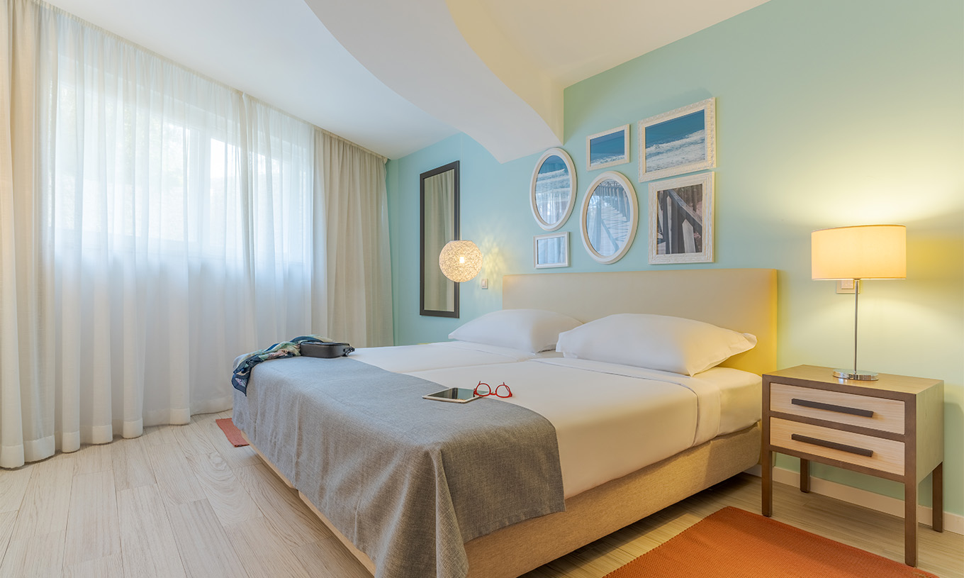 La Suite T1 Vista Jardín del Pestana Alvor Praia tiene dos camas juntas, mesa de noche con lámpara, alfombra y cuadros