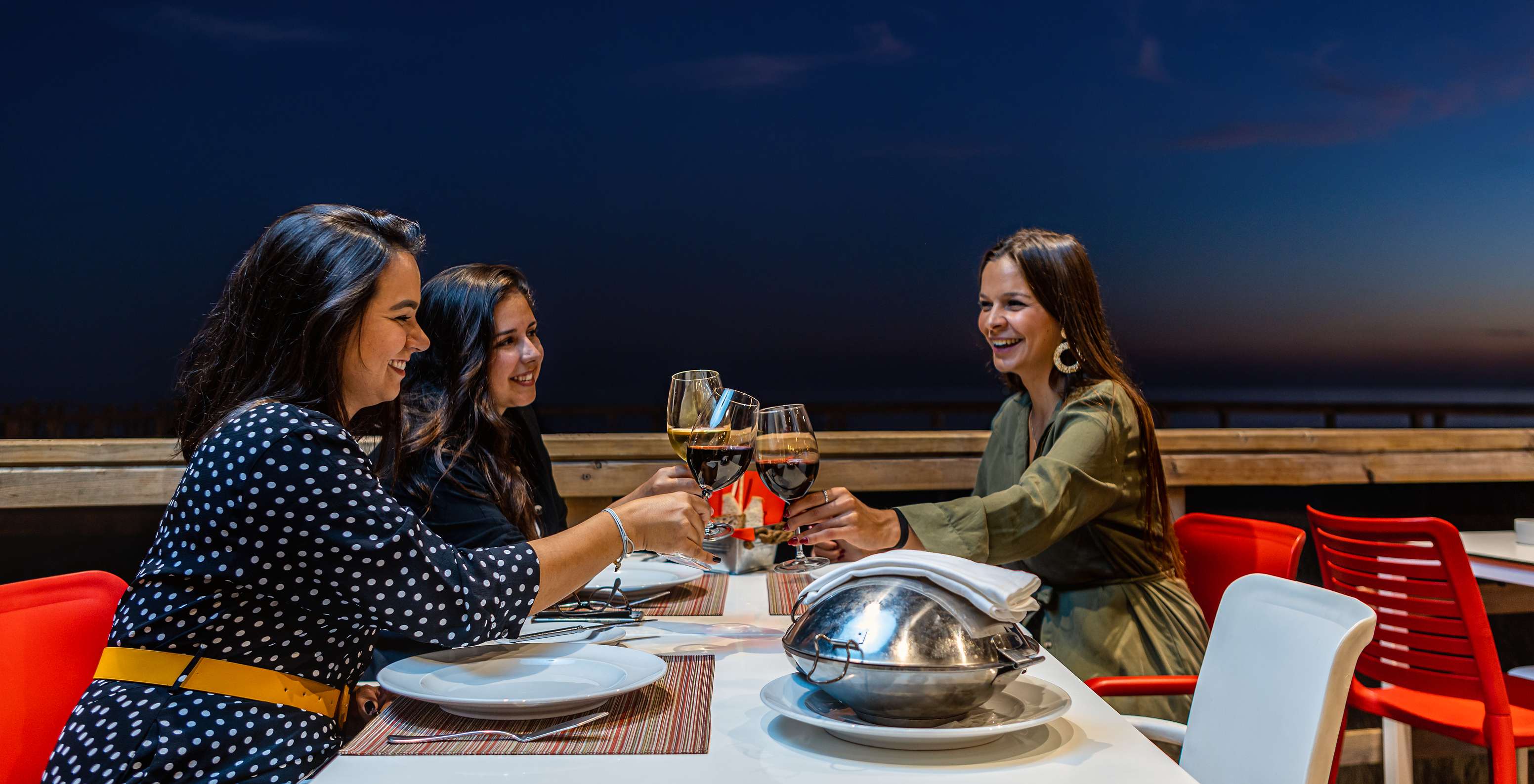 Amigas brindan y disfrutan de una deliciosa cena y una copa de vino en la terraza del restaurante Sea Deck