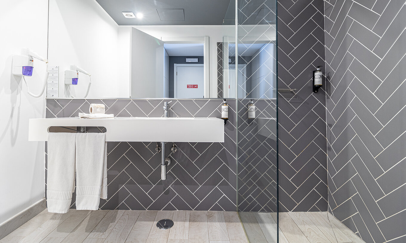 La Habitación Clásica Vista Piscina tiene baño moderno con lavabo blanco, espejo y ducha de vidrio