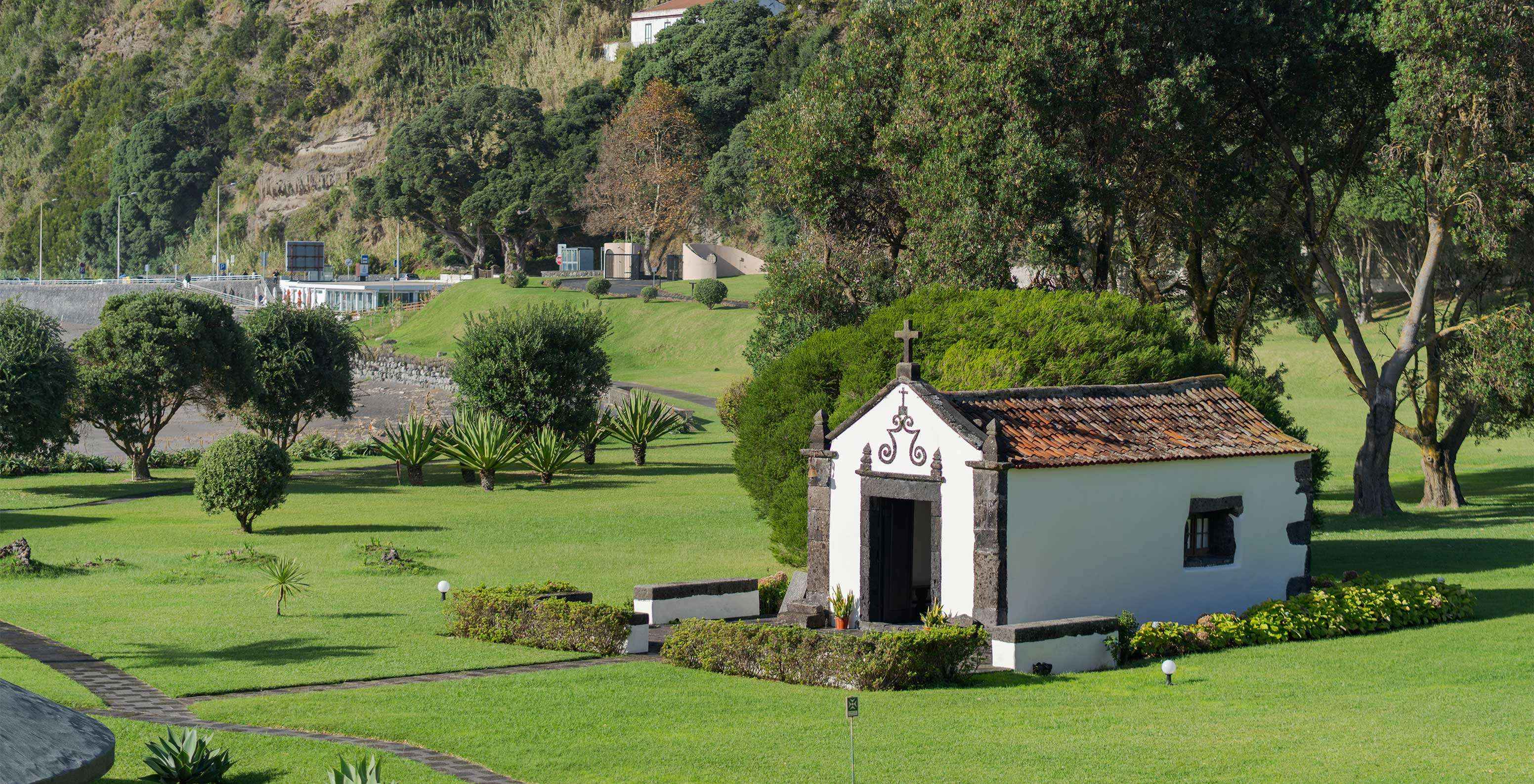 Capilla en el exterior del hotel, en medio de jardines verdes con árboles y pequeños paseos para los clientes