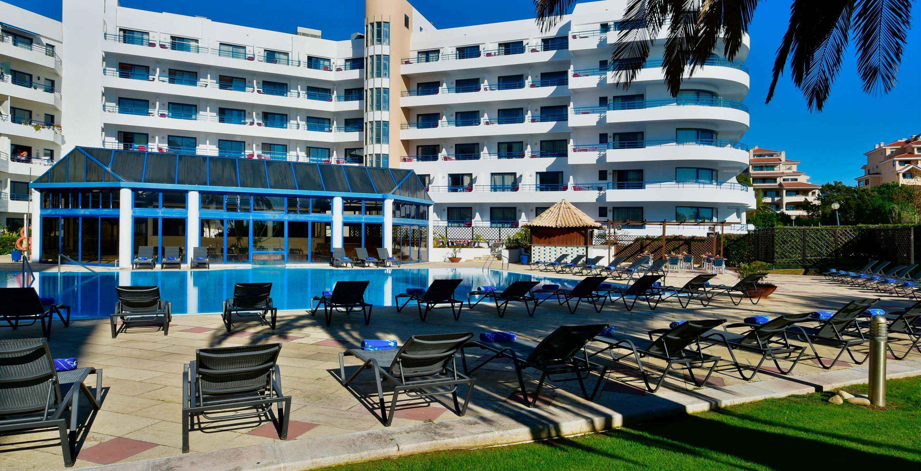 Vista del jardín del Pestana Cascais hacia la piscina exterior, tumbonas y el bar de la piscina