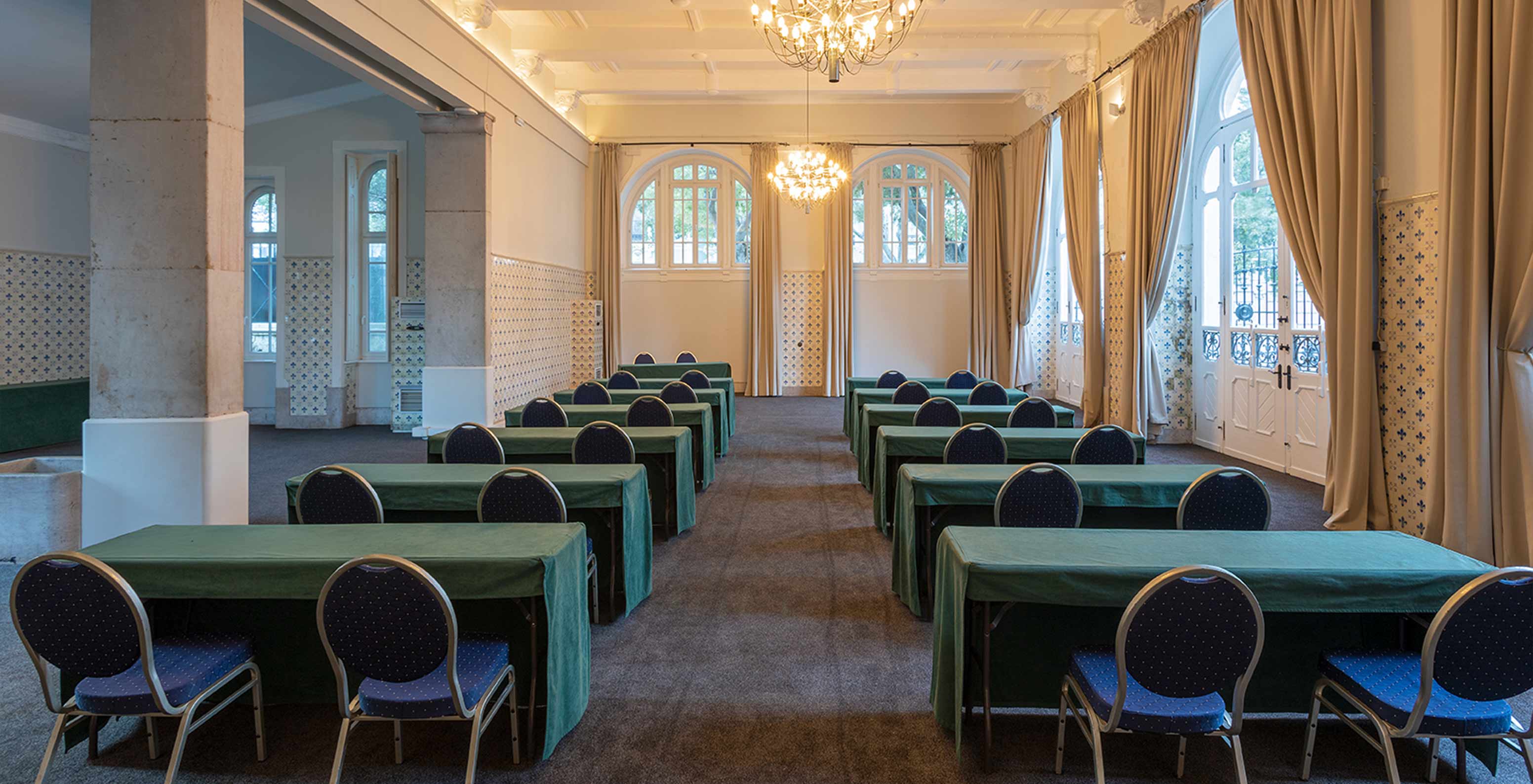 El Pestana Palace Lisboa tiene una sala de reuniones con mesas largas verdes, sillas azules y varias ventanas