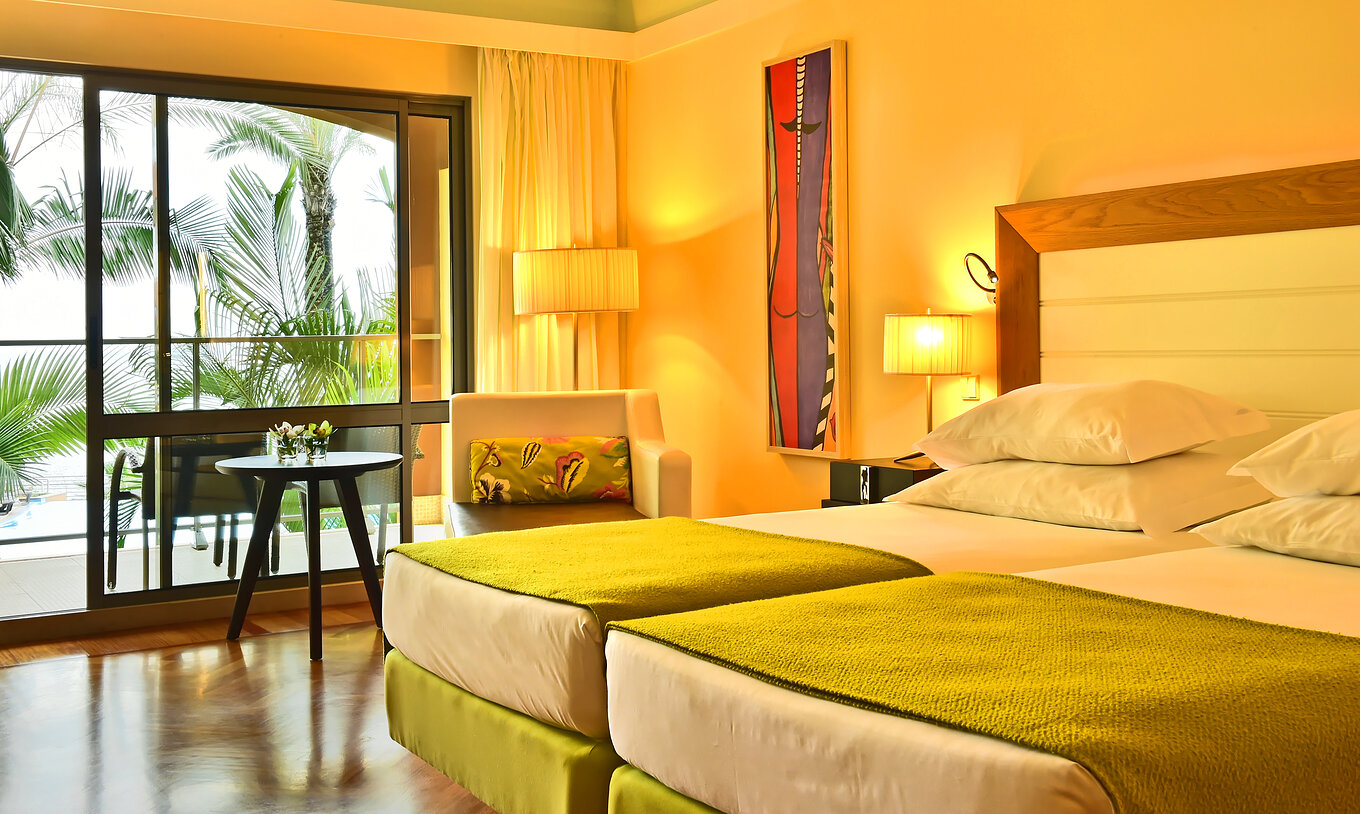 El Clásico Vista Piscina del Pestana Promenade tiene dos camas con un edredón verde y una ventana grande al balcón