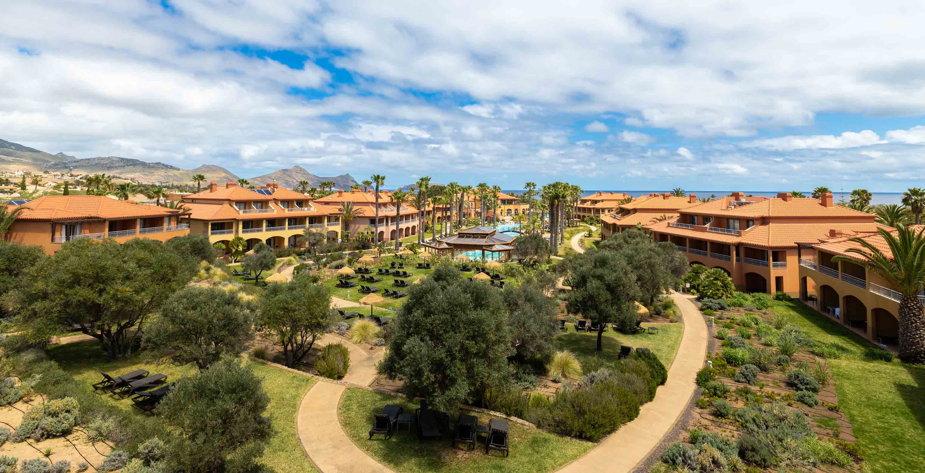 Jardines del Pestana Porto Santo All Inclusive con césped, palmeras tropicales, tumbonas y villas alrededor