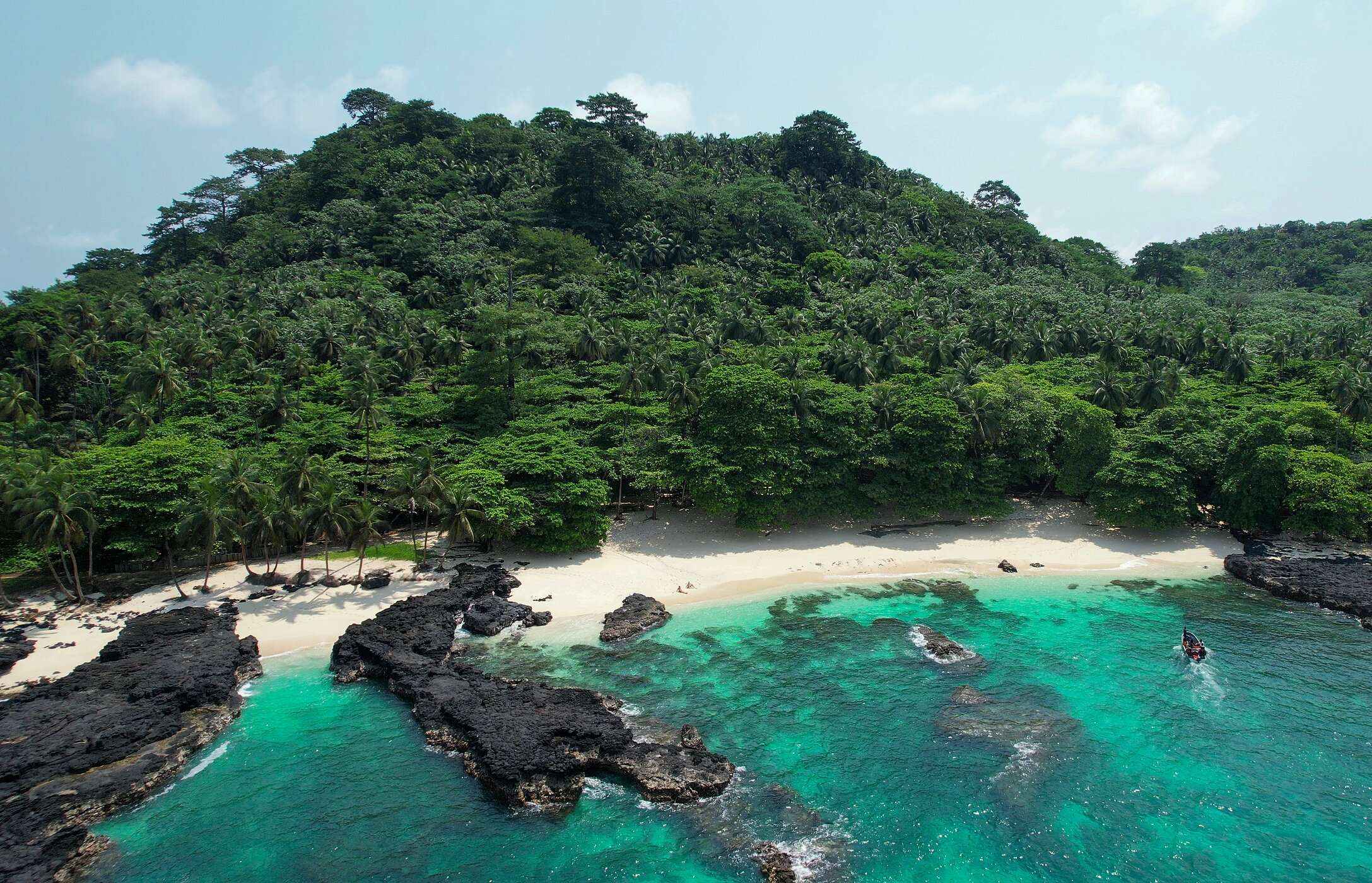 Praia Café, en la isla de São Tomé, desierta, con rocas tanto en la playa como en el mar, y una pared de vegetación